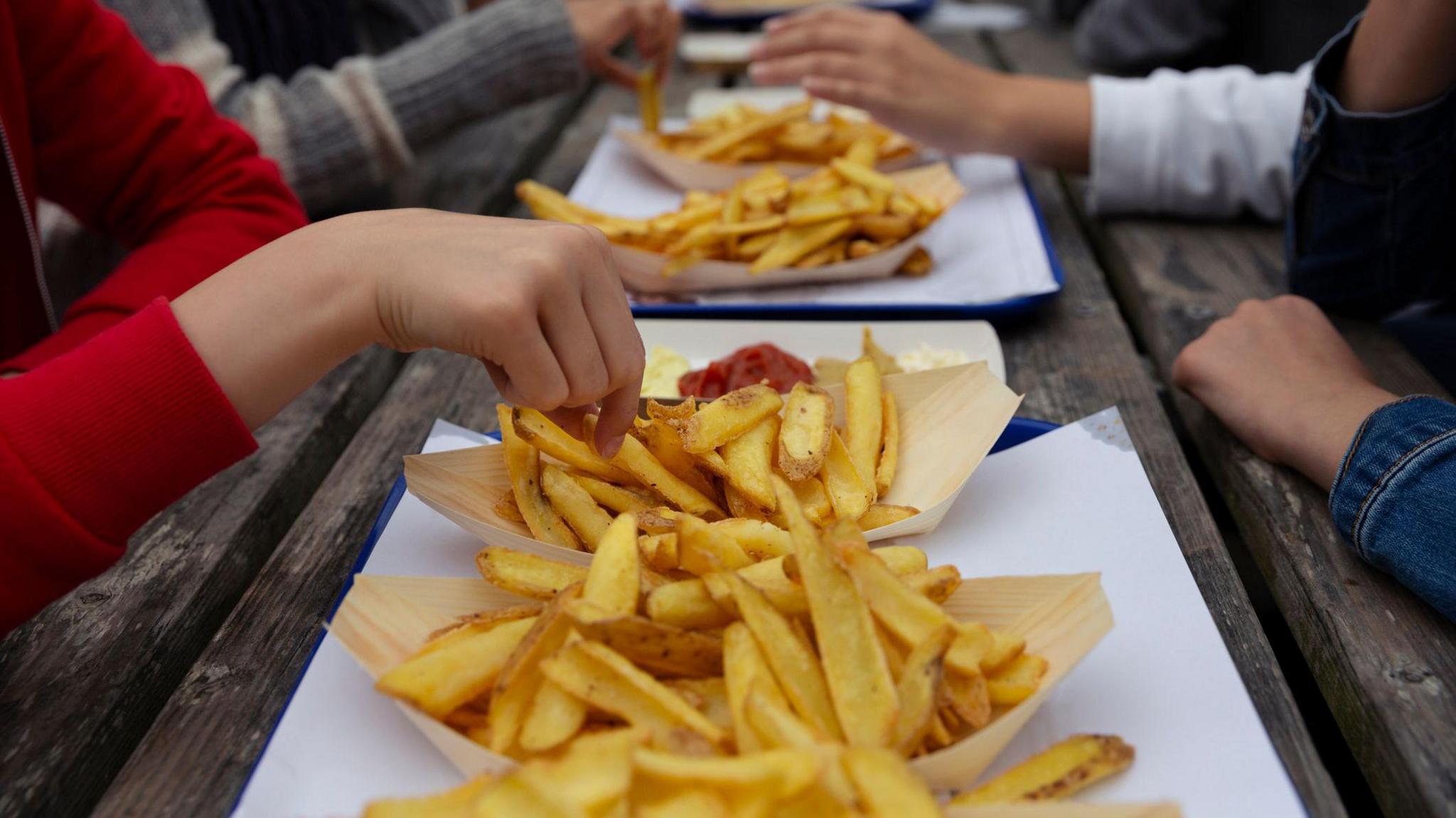 Row of takeaway chips on a picnic bench.