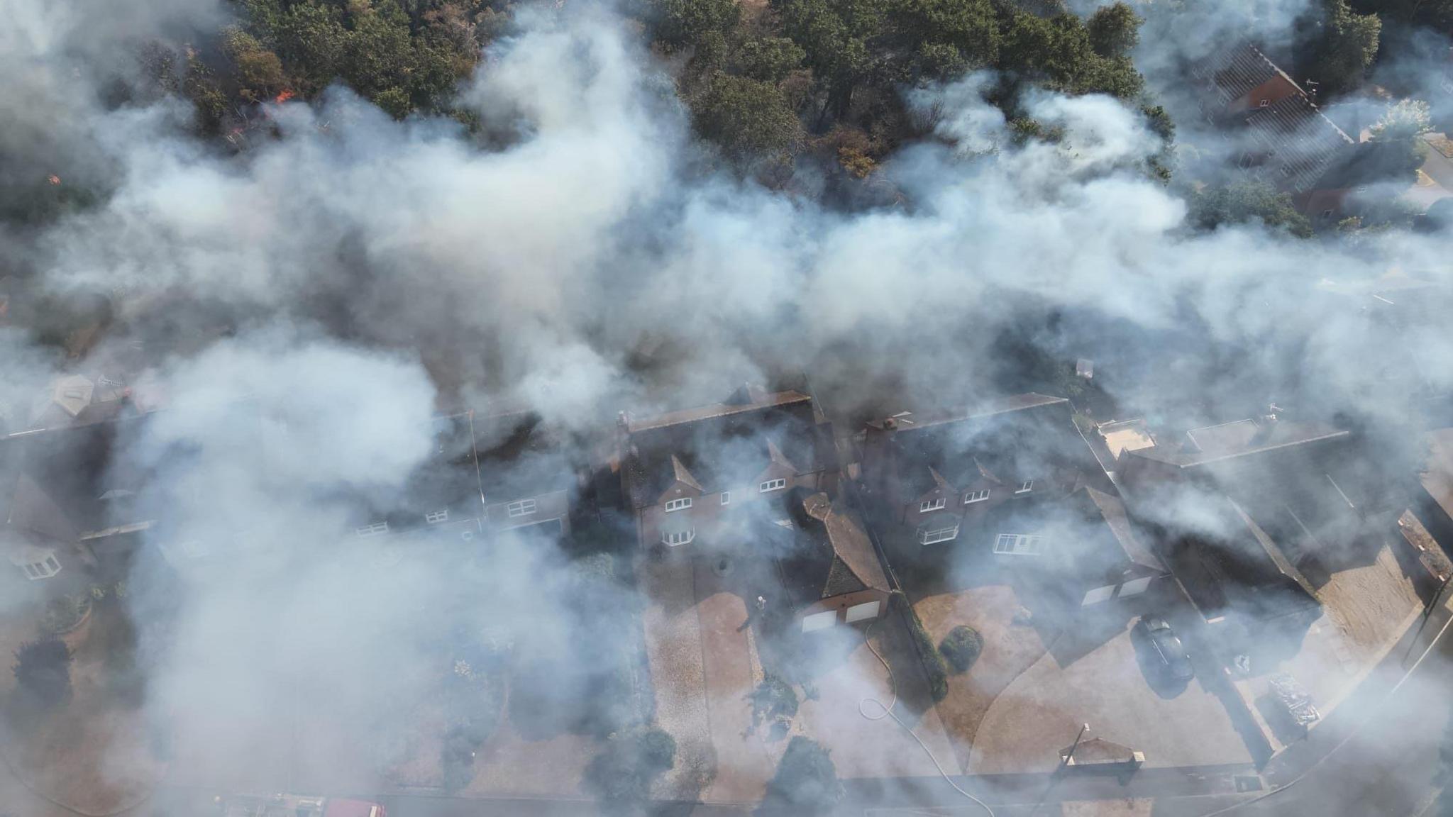 An aerial image of houses with large amounts of grey smoke over them.