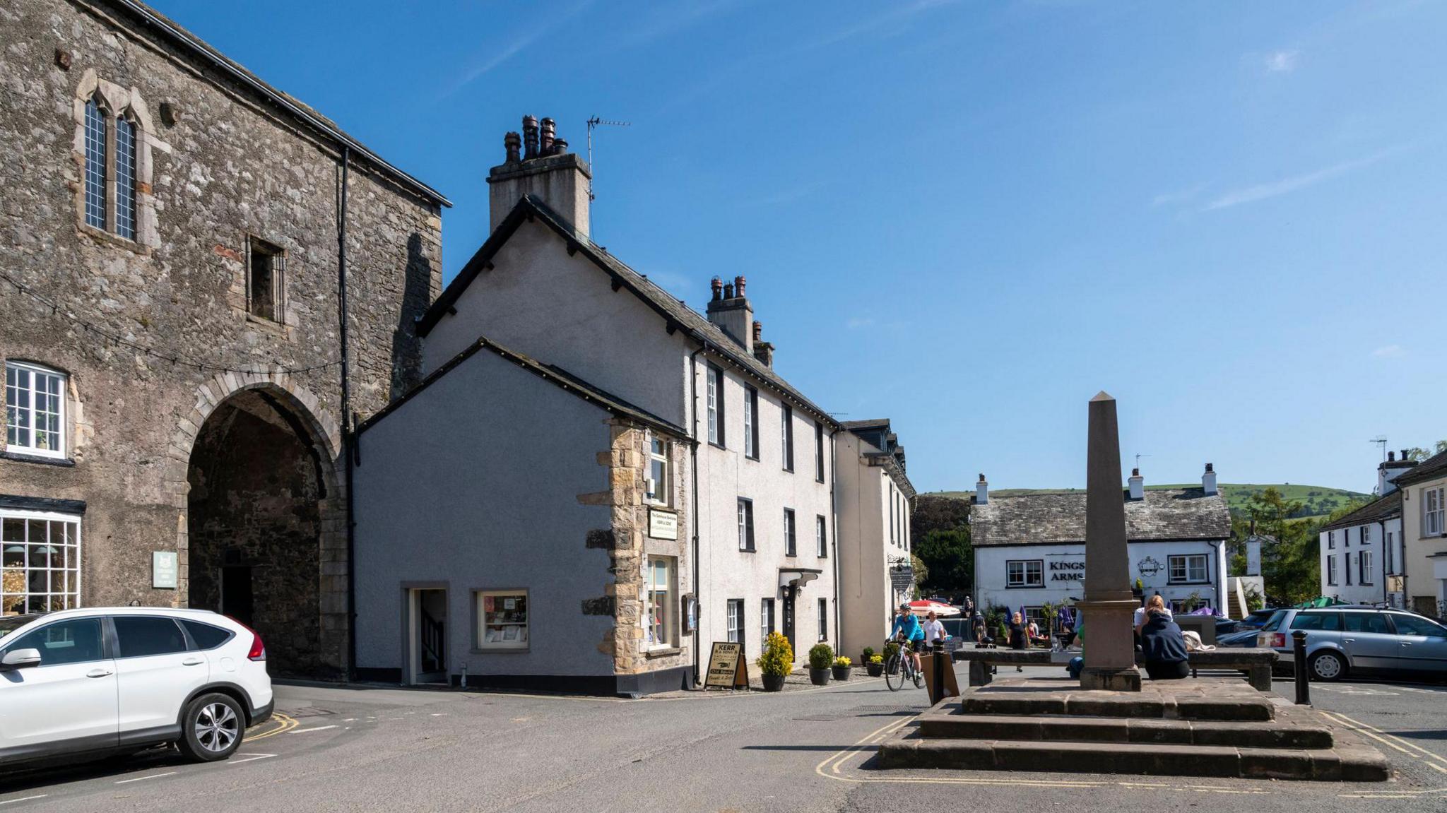 The main square of Cartmel, surrounded by stone buildings, shops and pubs, with a cenotaph in the centre.