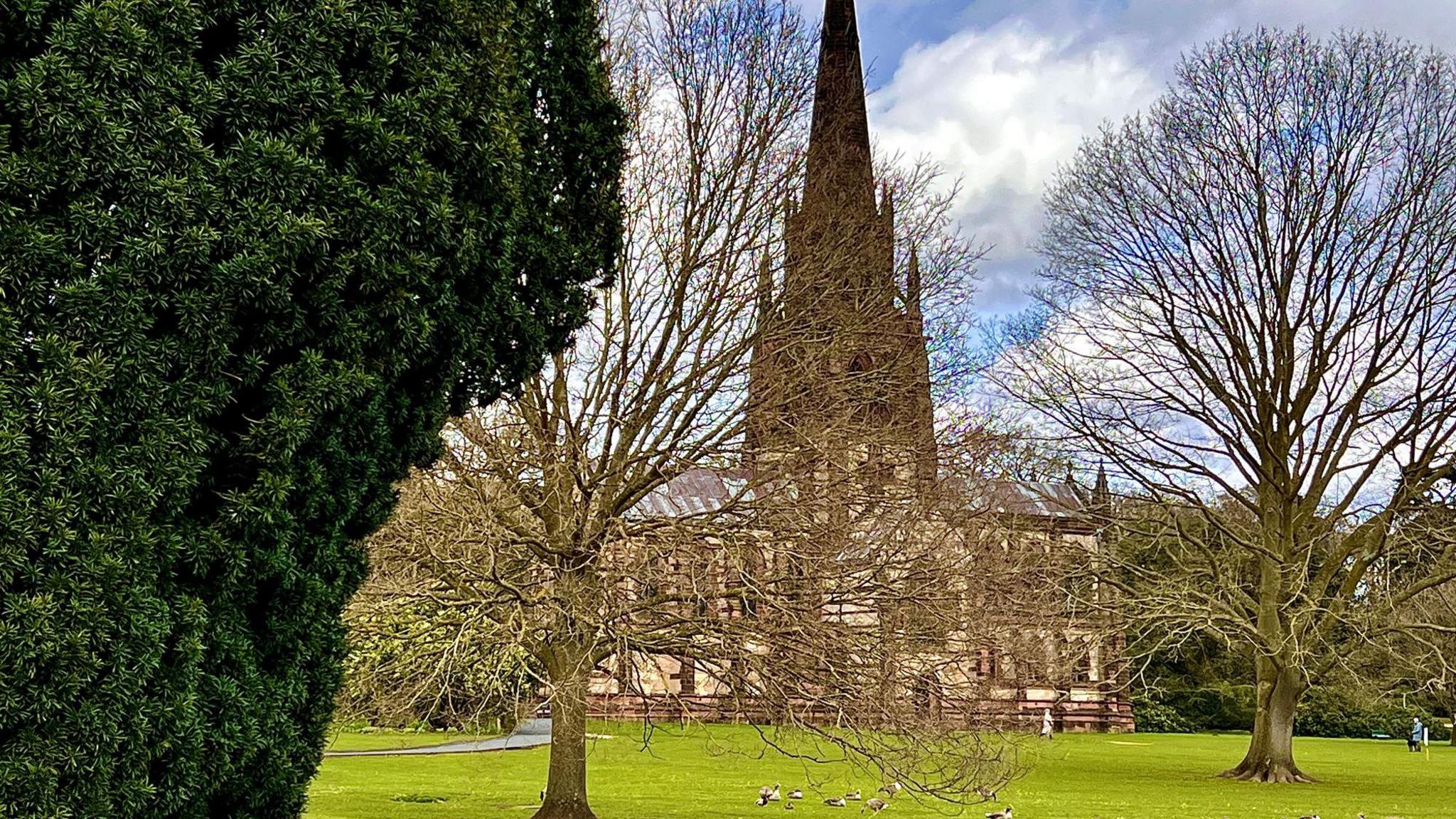 The large Victorian spired church at Clumber Park, seen through trees across an area of park grassland