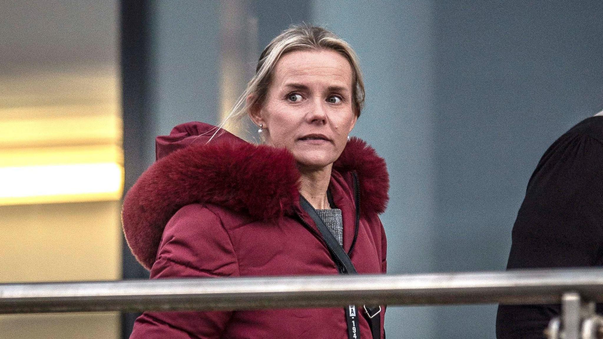 Emma Gardner, a blonde woman with her hair tied back. She has a red coat on with a red fur hood.