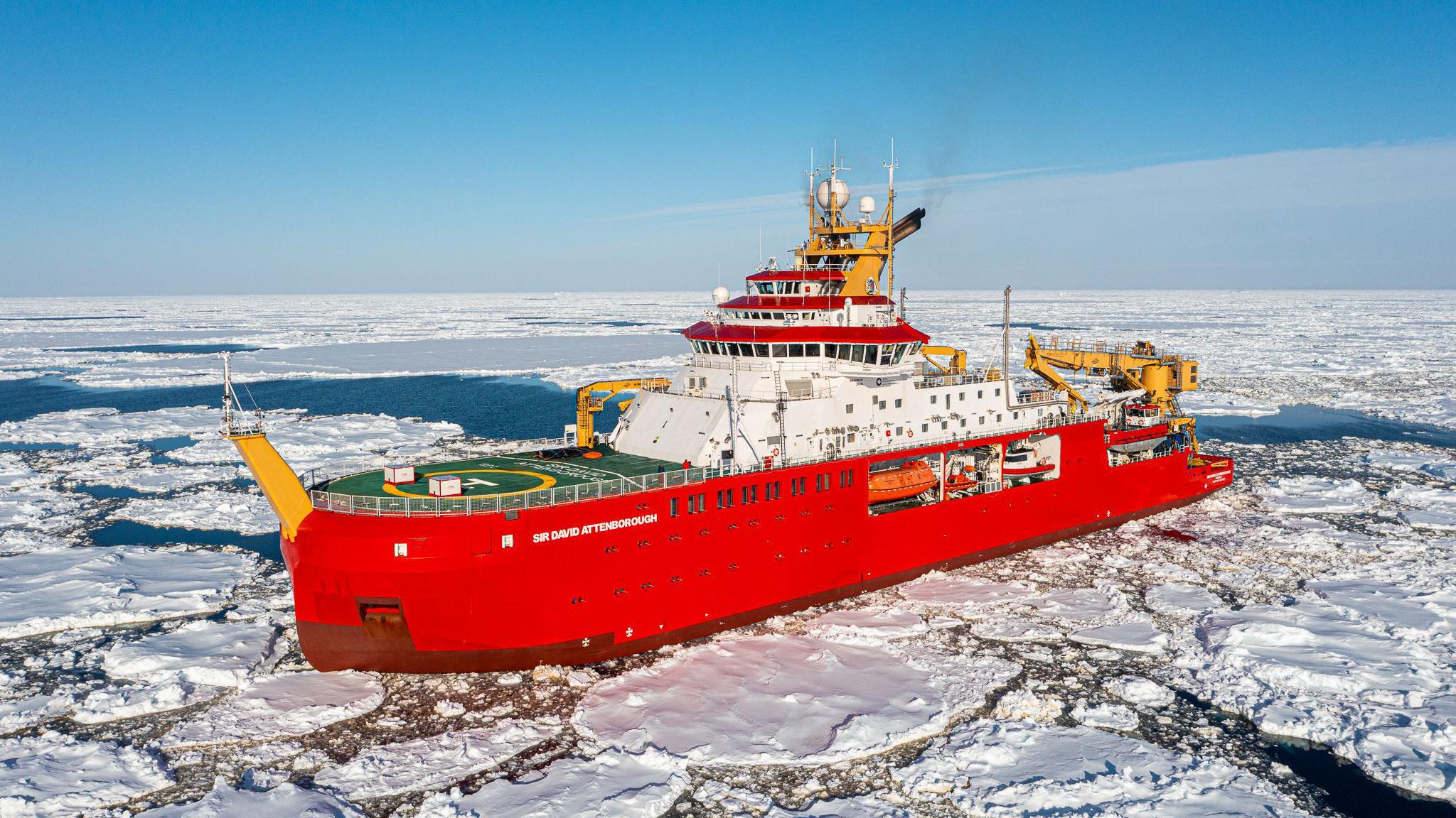 A red ship in the ocean surrounded by ice. On the side of the ship are the words "Sir David Attenborough" in white letters.