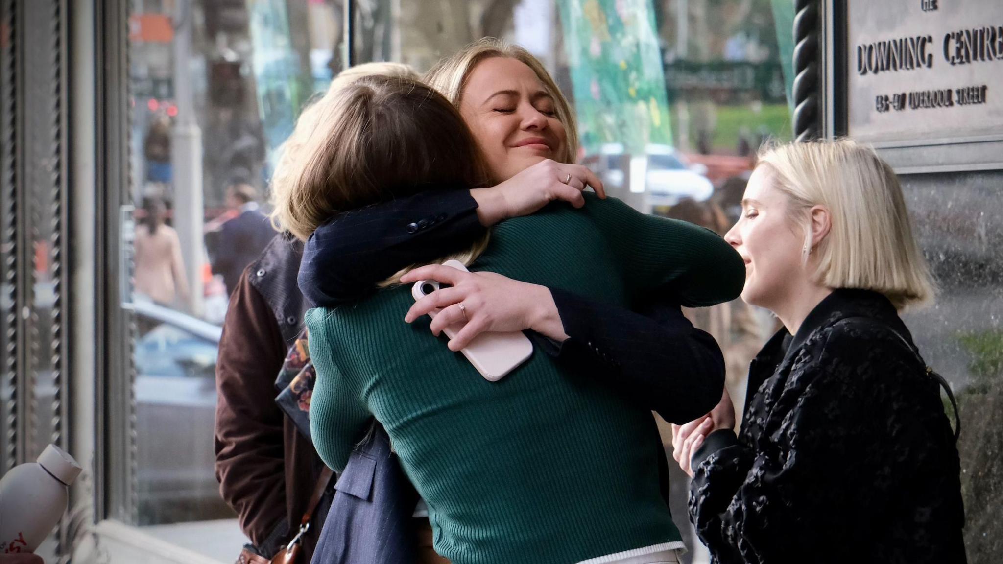 Two women are hugging. They are stood outside a building