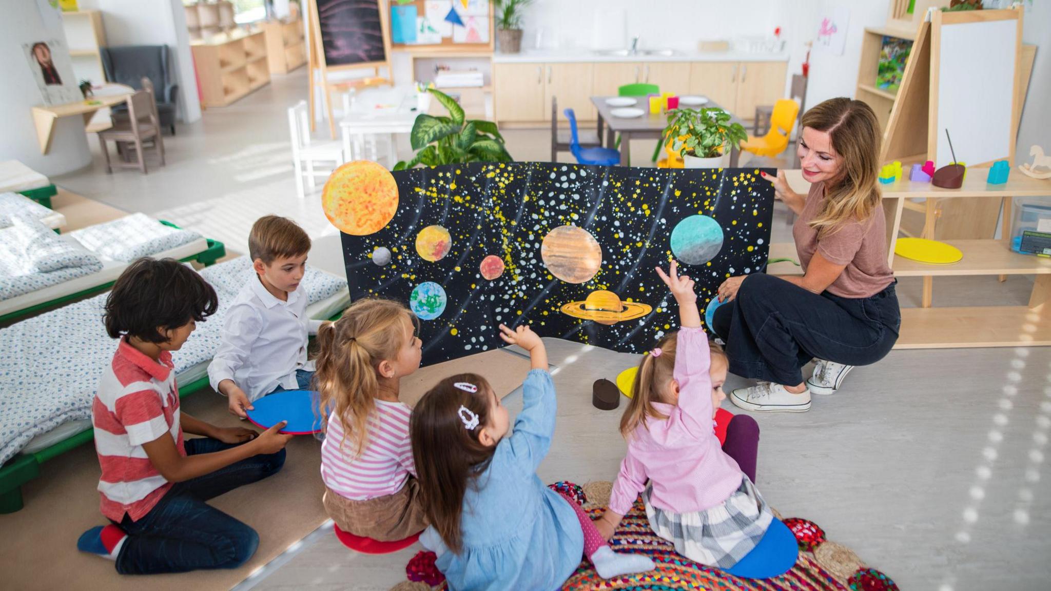 Teacher and young children at a childcare centre. The kids are looking at a drawing of the solar system. 