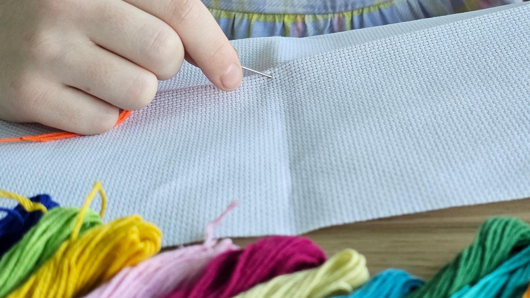 A child's hand holding a needle with coloured embroidery threads at the foreground