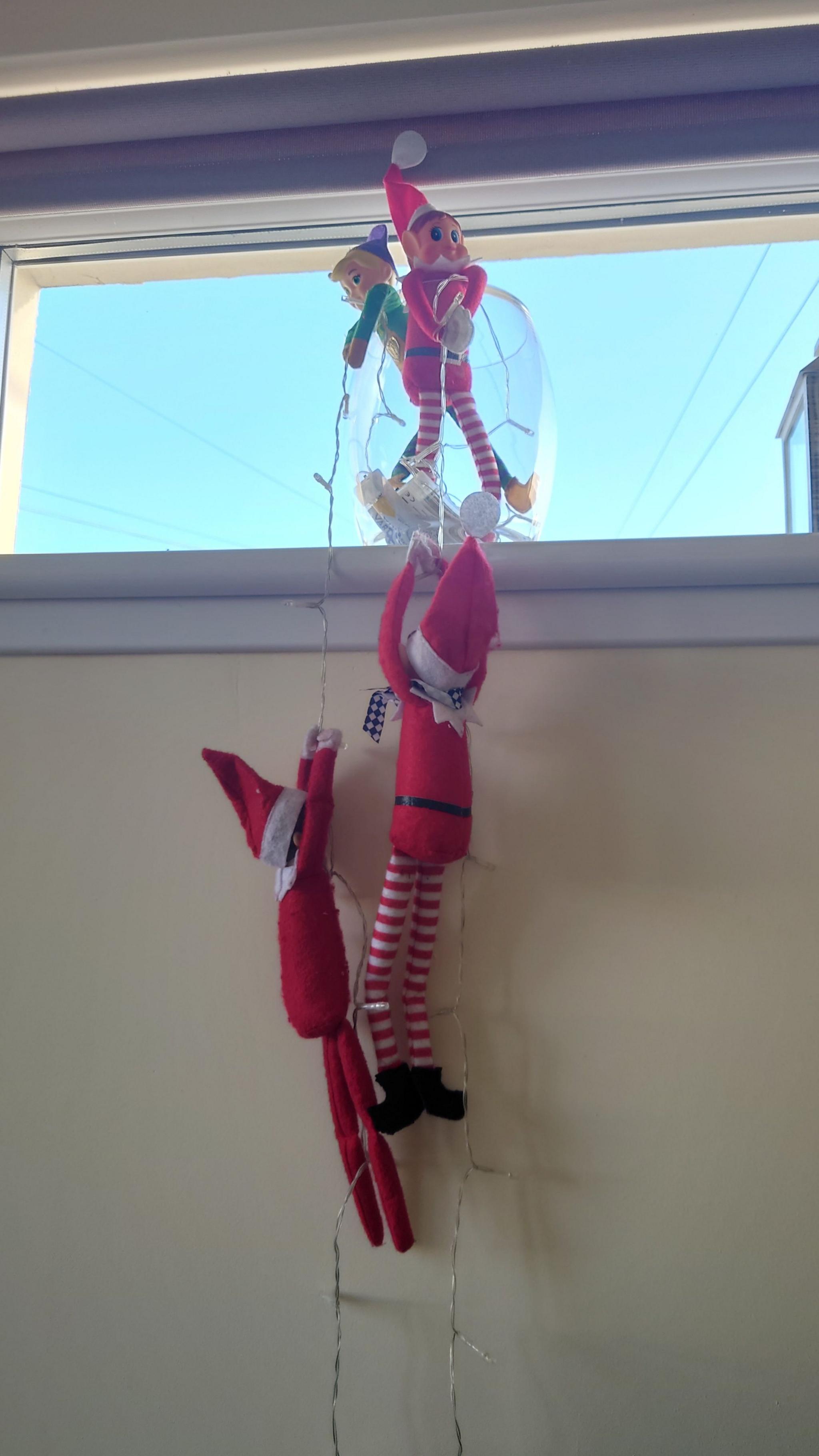 Plastic elves can be seen on windowsill hanging off while holding onto some fairy lights 