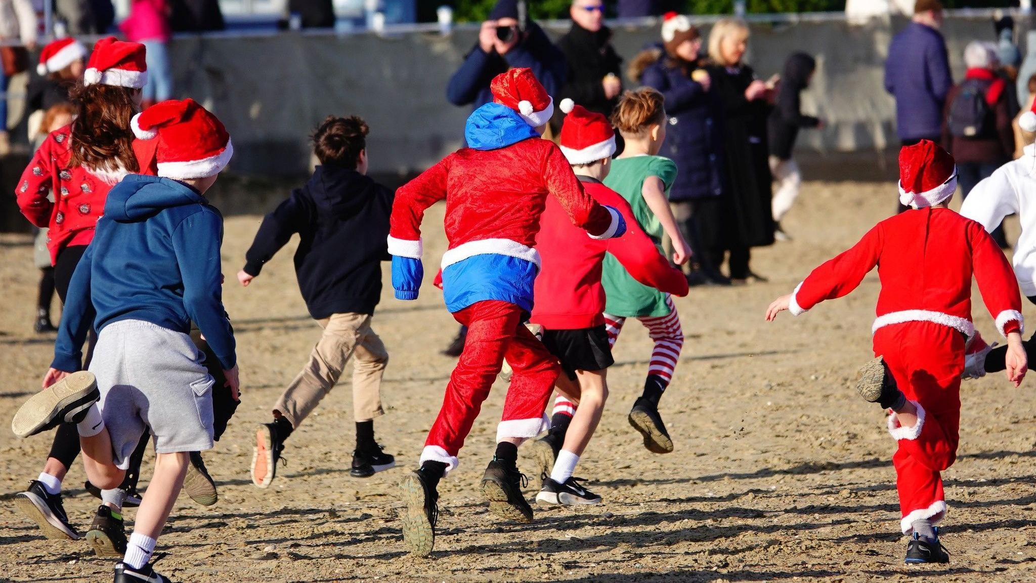 Children dressed as santa and elves running on the beach