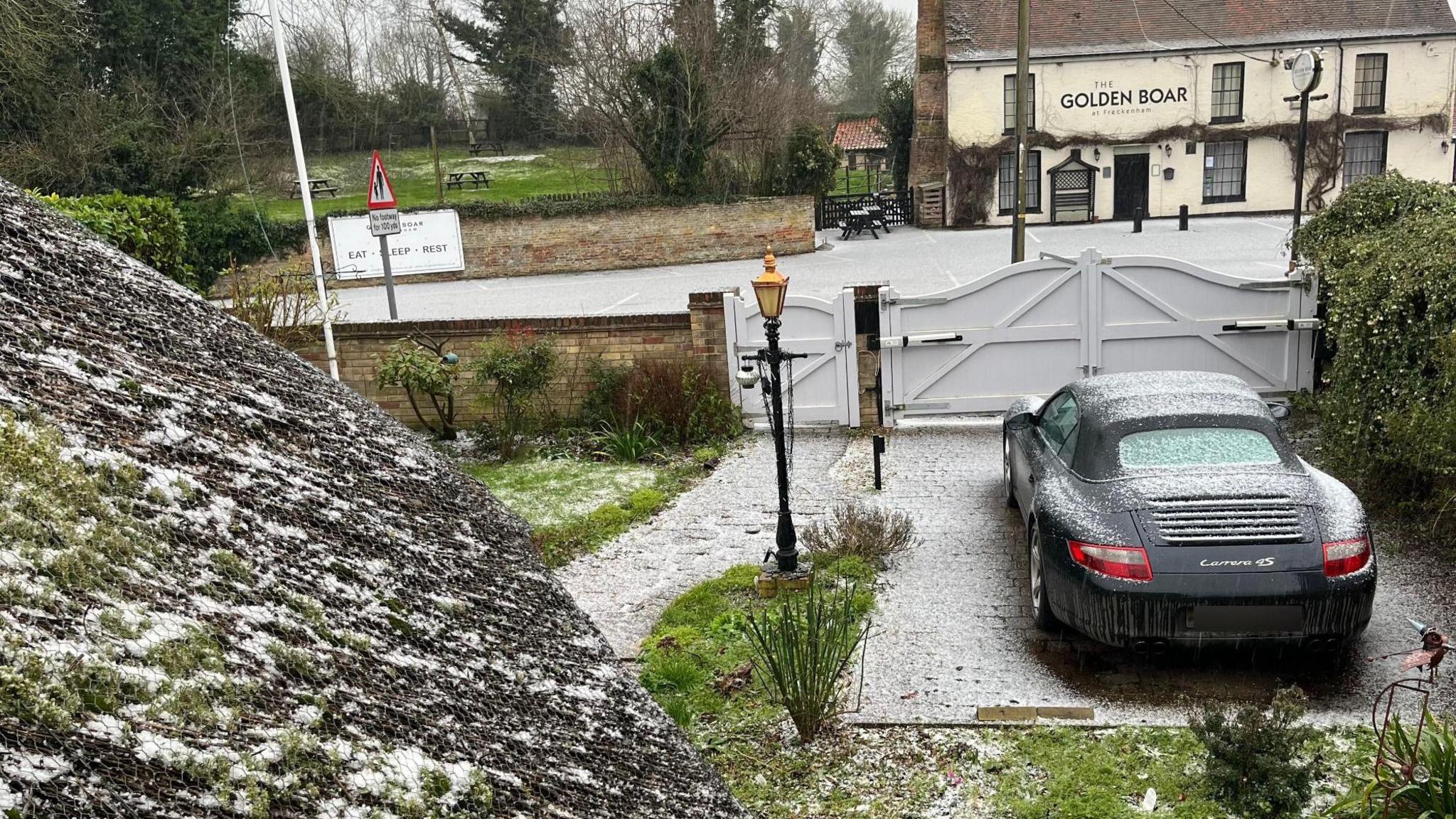 Hail on a driveway in Suffolk. A pub is visible in the background.