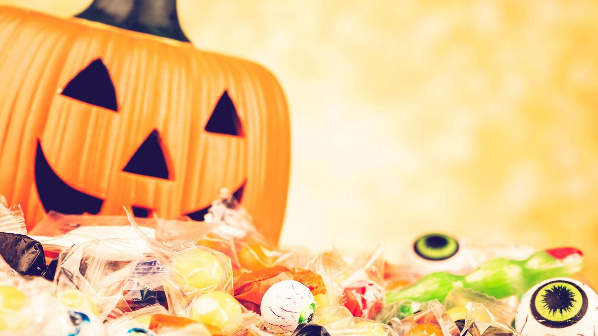 A picture of a pumpkin with a carved face and sweets,