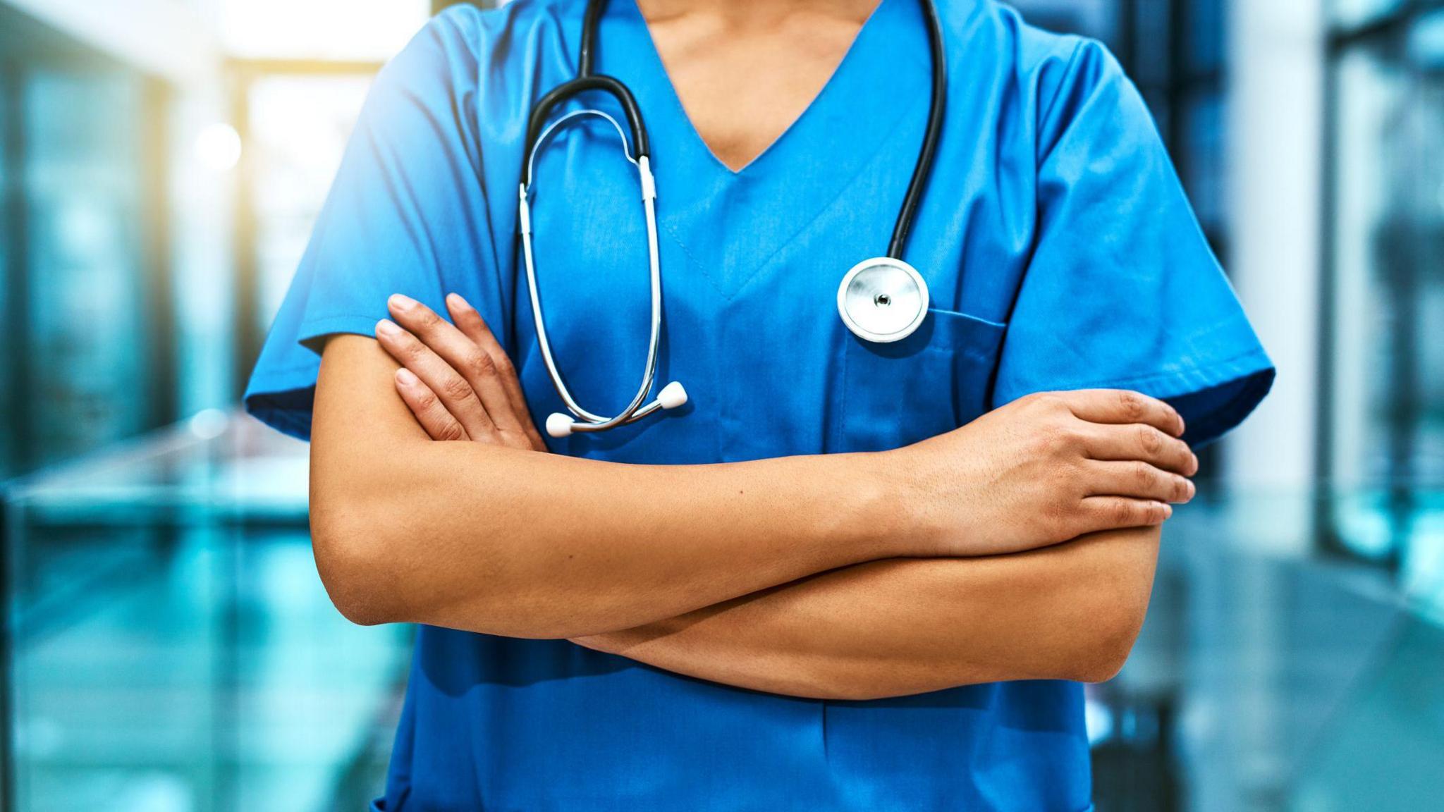 Shot of an unrecognisable female nurse standing in a hospital. She wears blue scrubs and has a stethoscope