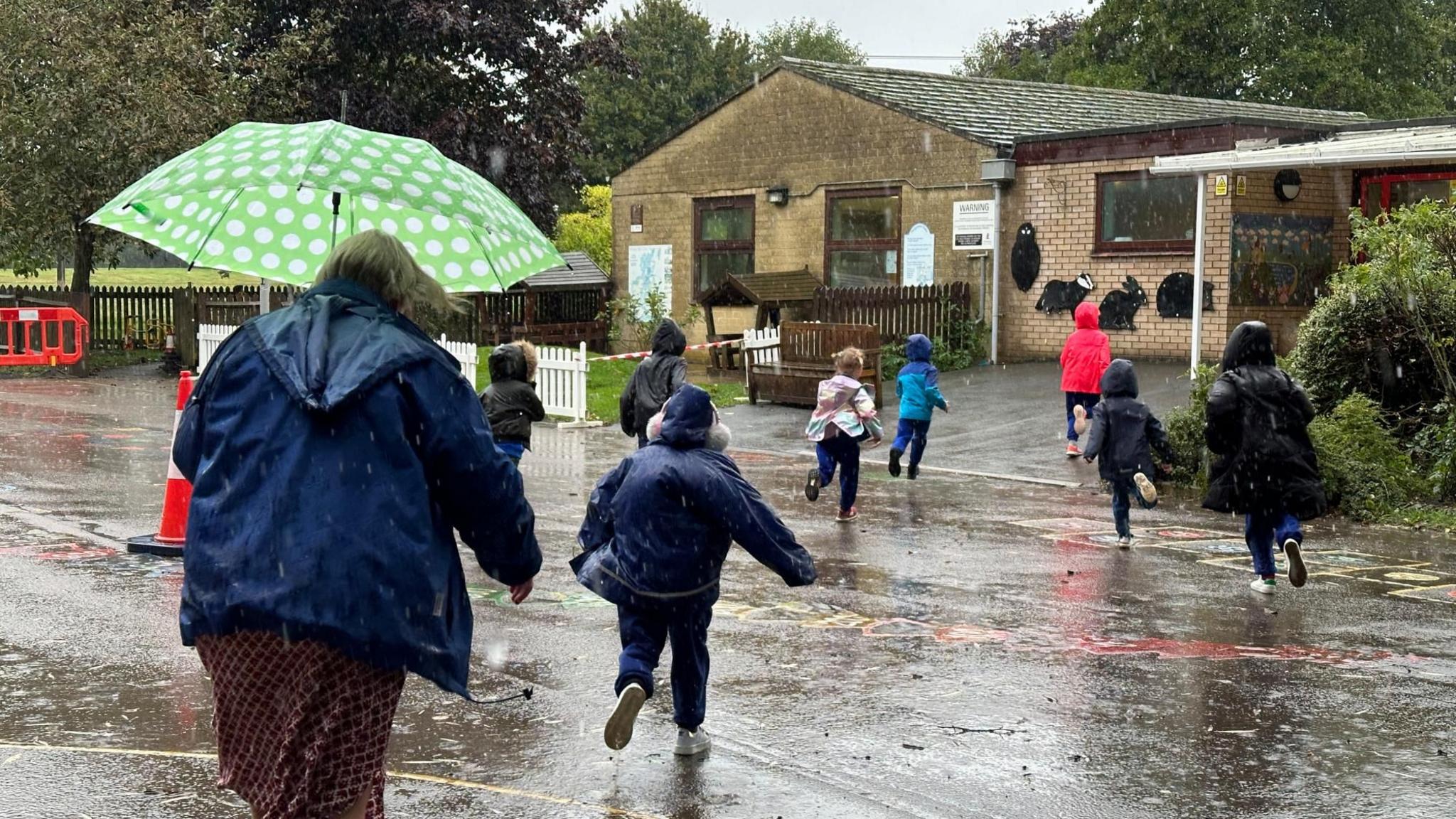 Children wearing coats and hoods run across a water logged playground to the safety of a school building as it rains