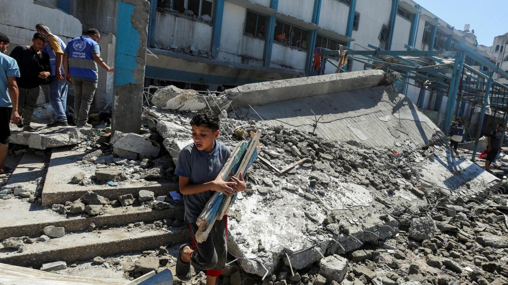 A Palestinian boy carries pieces of wood following an Israeli strike on a Unrwa-run school in Nuseirat refugee camp, in central Gaza (16 July 2024)