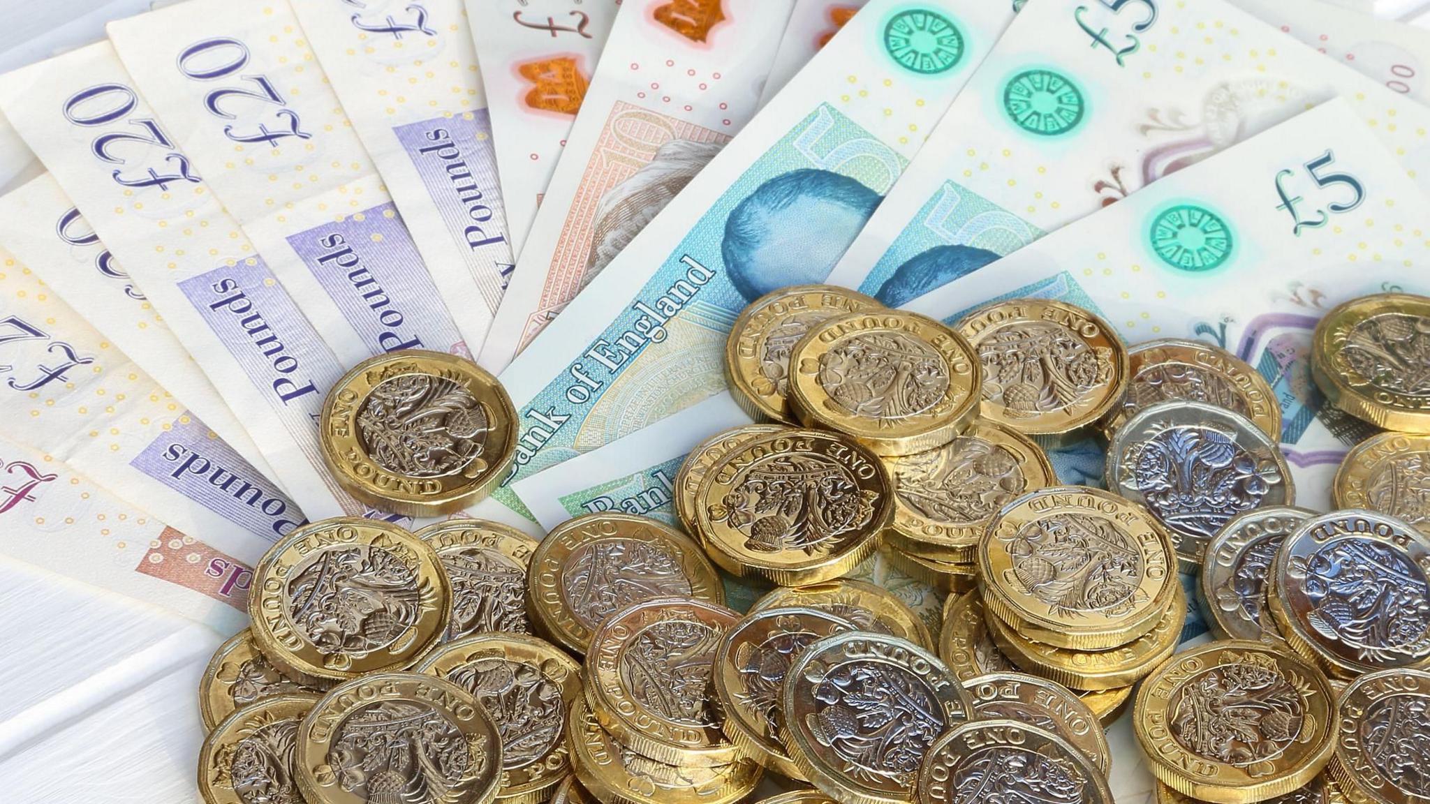 Assorted one pounds coins placed on a number of £20, £10 and £5 sterling notes.