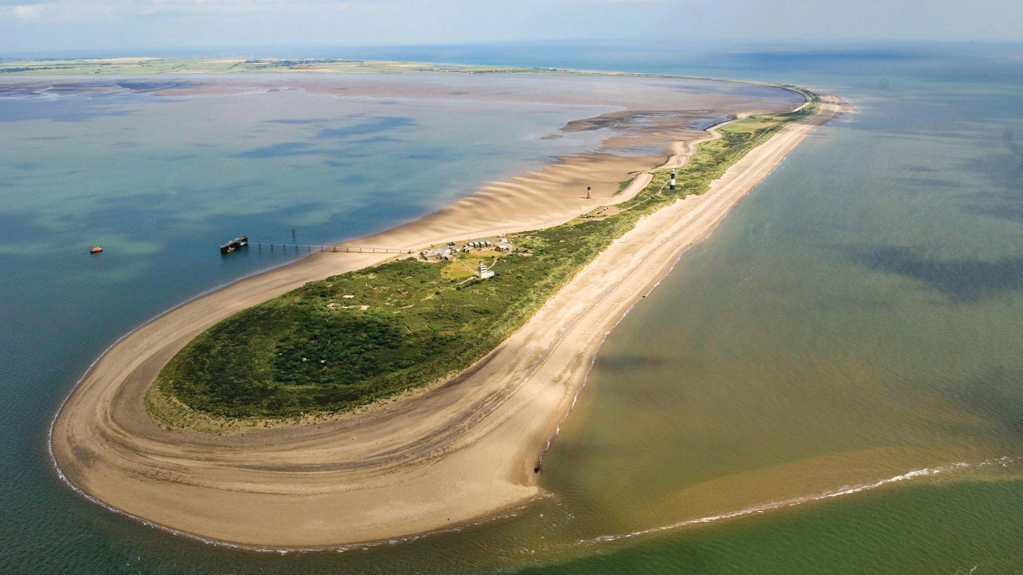 Aerial view of a Spurn Point - a long piece of land with greenery in the middle and sand on the edges. The river water is surrounding it.