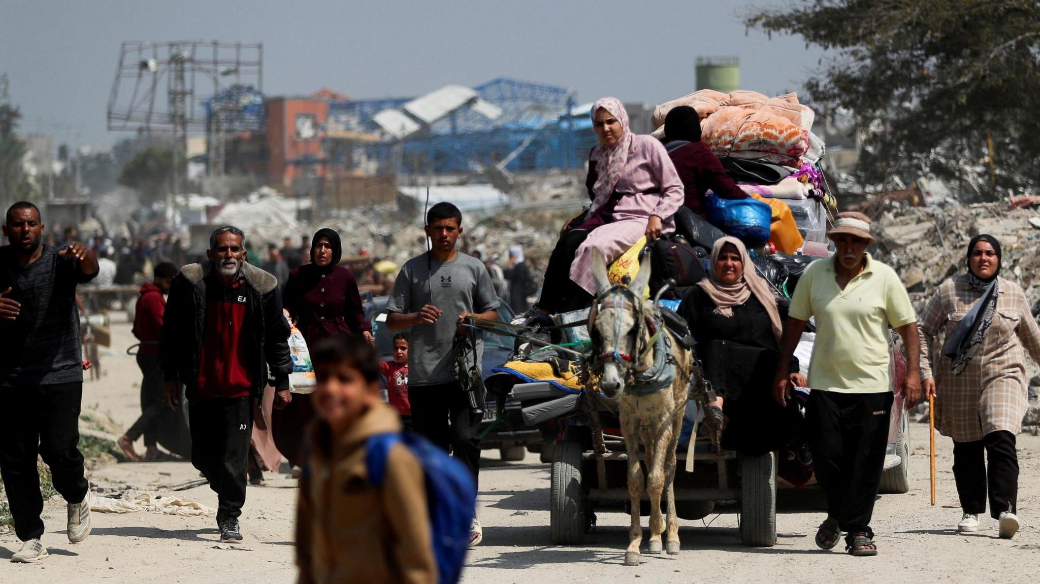 Gazans walking in a street carrying their belongings, along with a car led by a donkey 