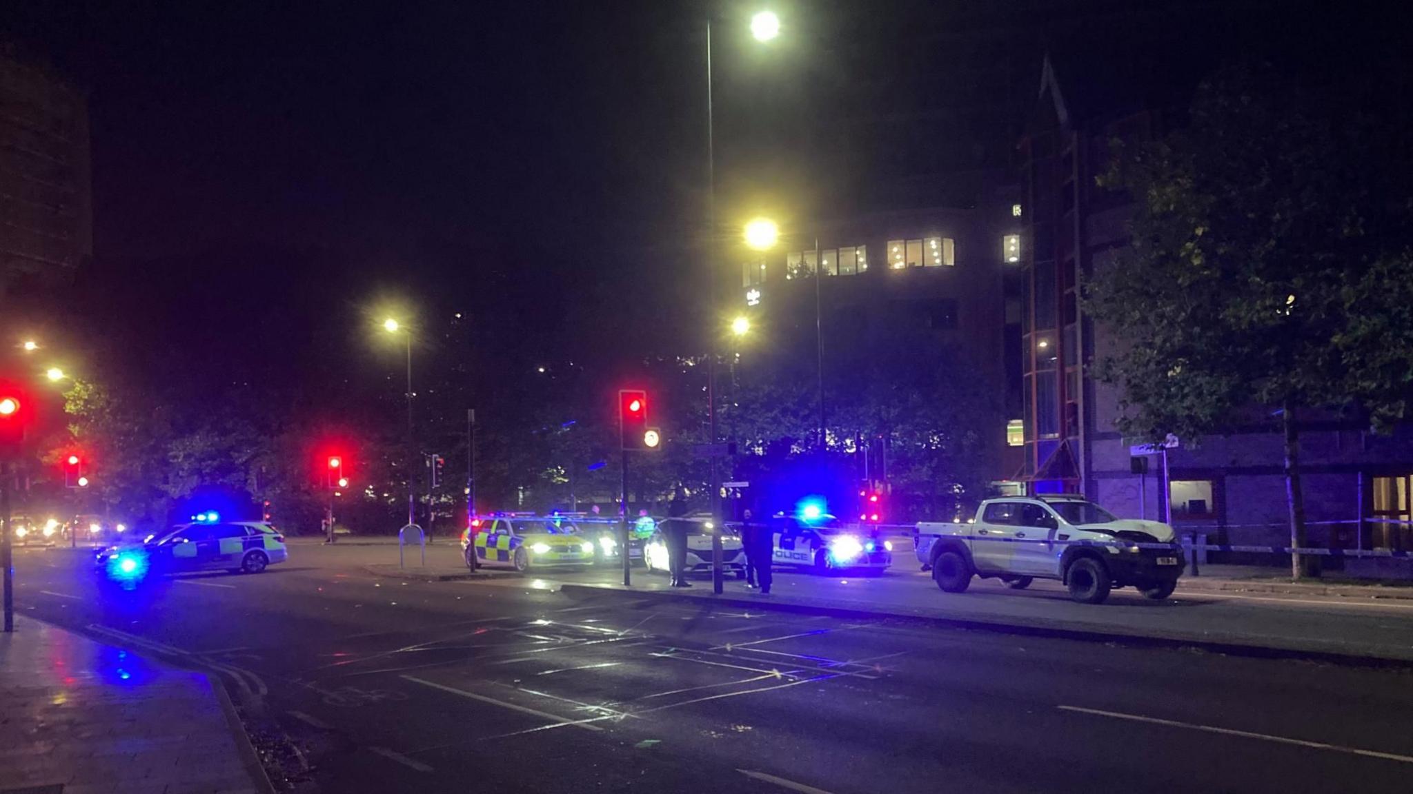 Police cars block off the northbound exit of the Civic Drive/Princes Street crossroads. A white SUV-type vehicle is pictured with the police cars. It is dark with street and traffic lights shining.