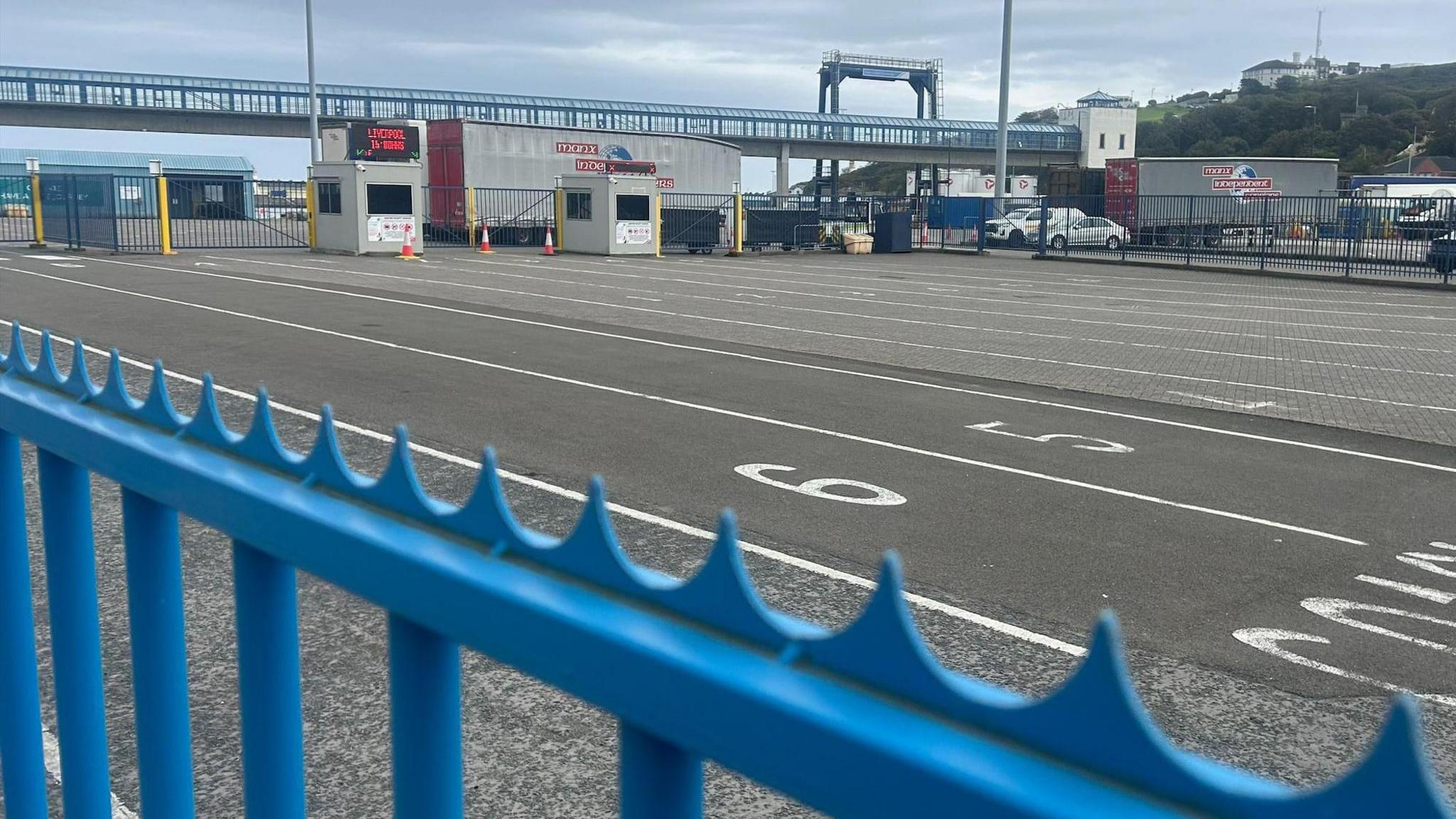 A large tarmacked area, with white painted lines to create numbered lanes for vehicles to park. It is empty and there is a blue railing in the foreground.