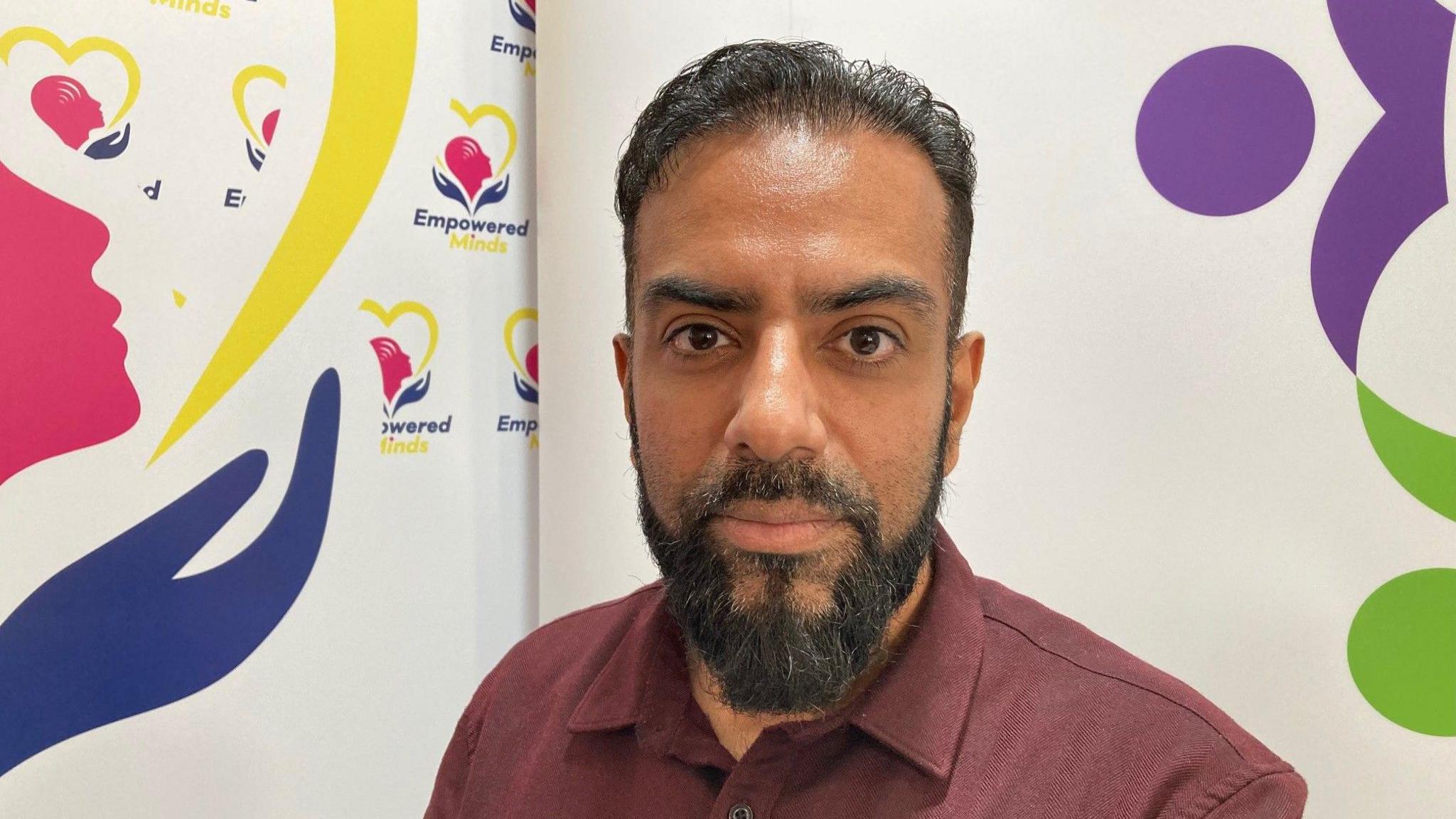 Abbas Najib from Better Communities Bradford in front of poster with Empowered Minds written in blue and yellow lettering on it.