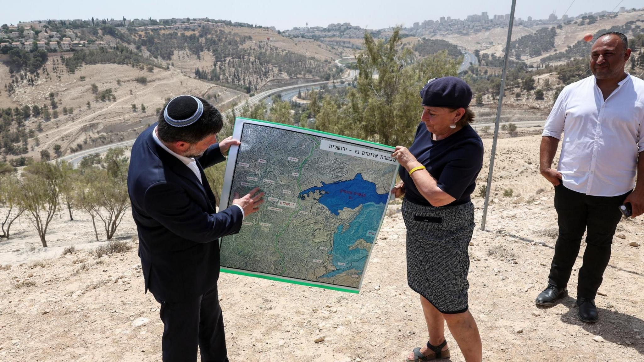 Israeli Finance Minister Bezalel Smotrich (L) helps to hold up a map showing the plans for the E1 settlement project during a visit to the area, in the occupied West Bank, on 14 August 2025
