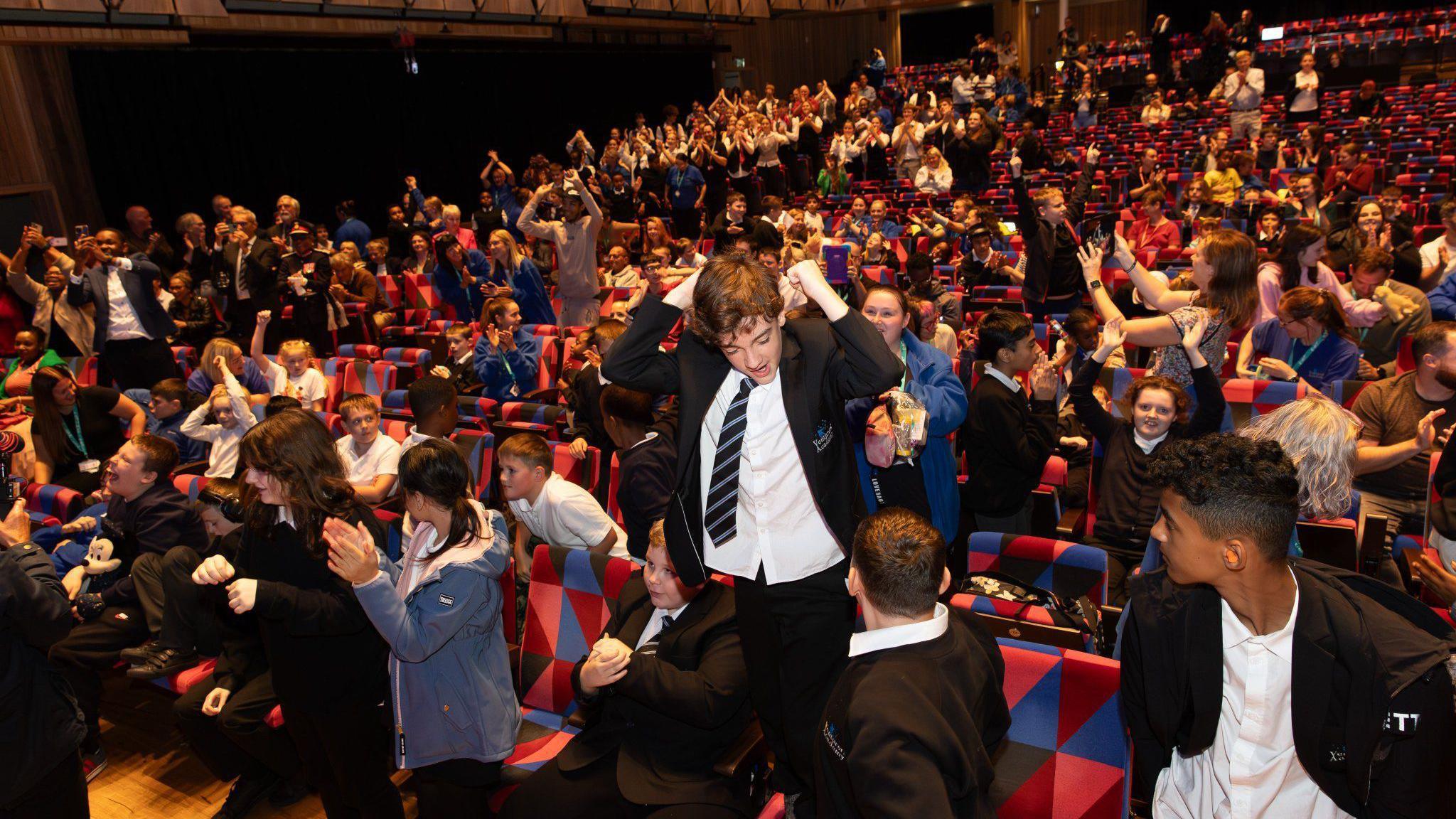 Hundreds of school pupils from Venturers Academy in Bristol celebrate the moment their school won an award, at Bristol Beacon. They are inside the main auditorium at the venue