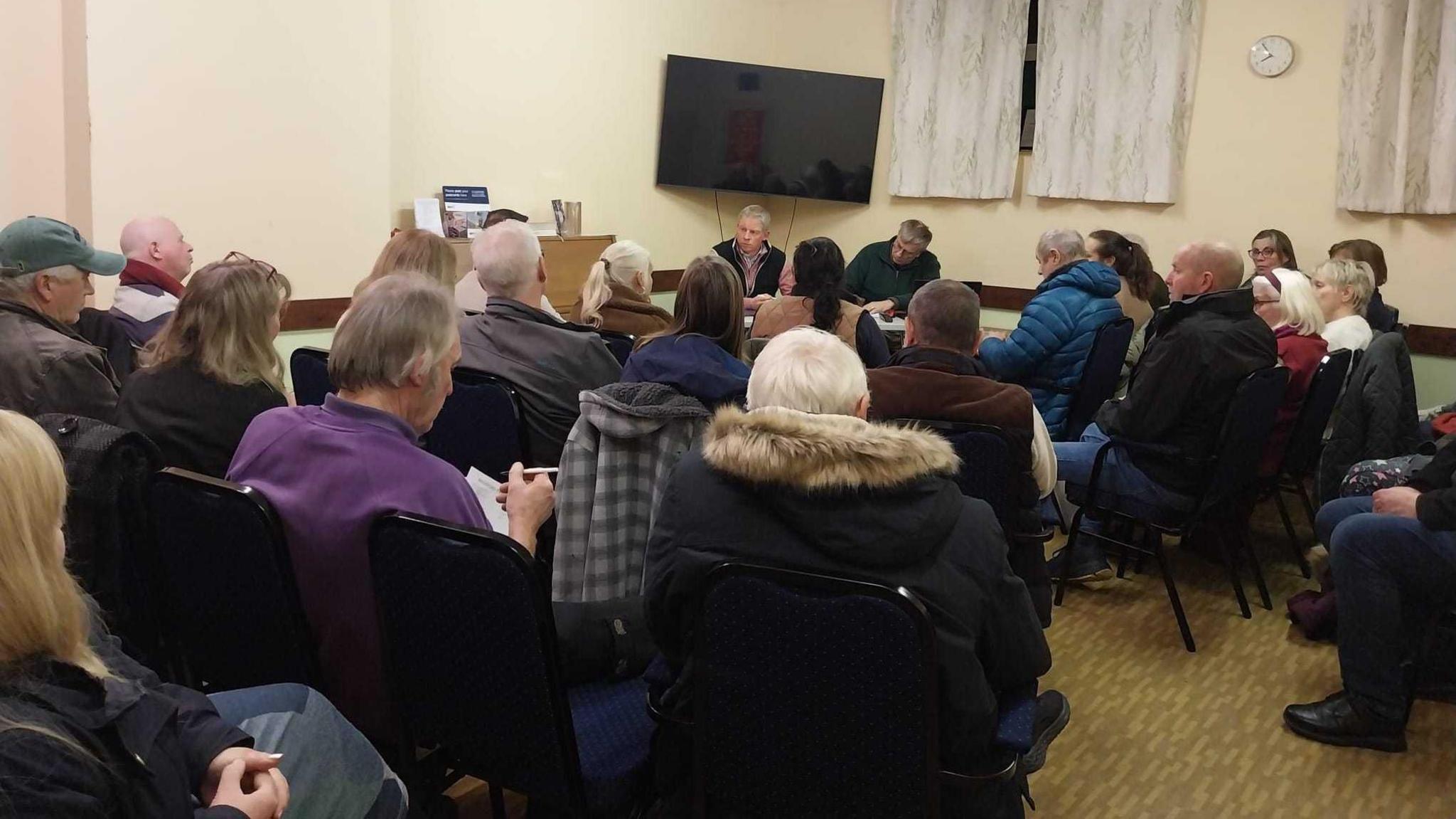A room full of people sitting down and listening to a man at the front.