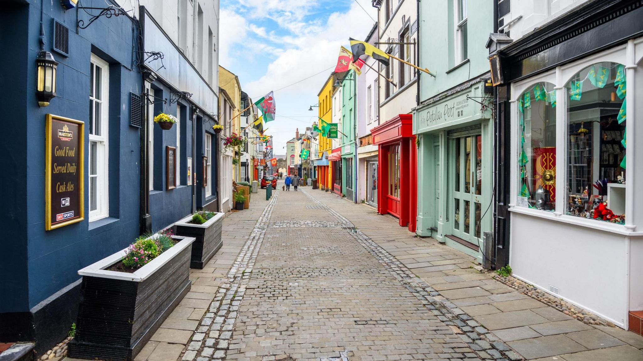 A stock photograph of Palace Street on Caernarfon, showing cobbled streets and different coloured shop fronts featuring flags