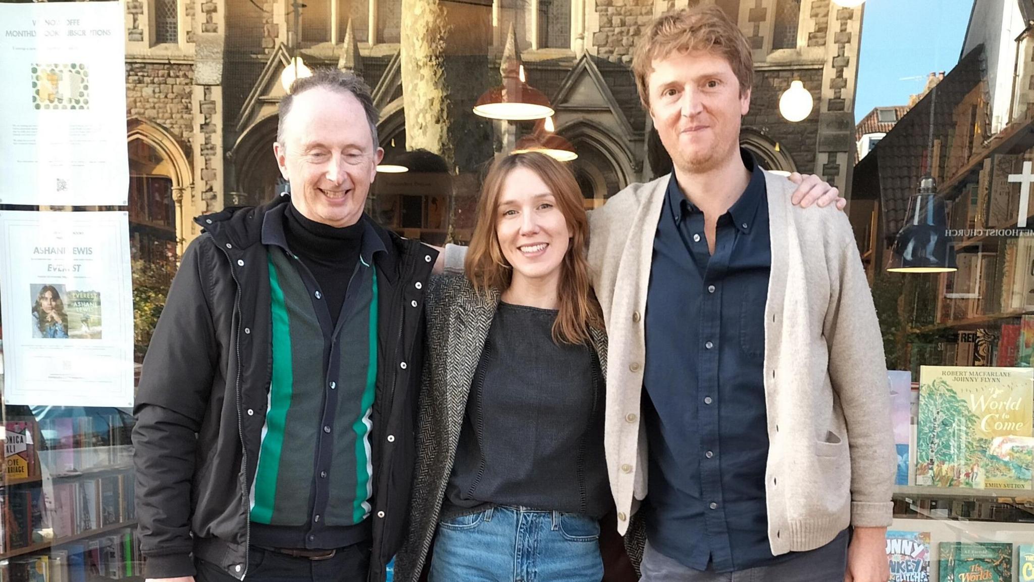 Three people, two men and a woman, stand outside a bookshop on Gloucester Road in Bristol. The woman, who is younger and has long brown hair, is standing in the middle