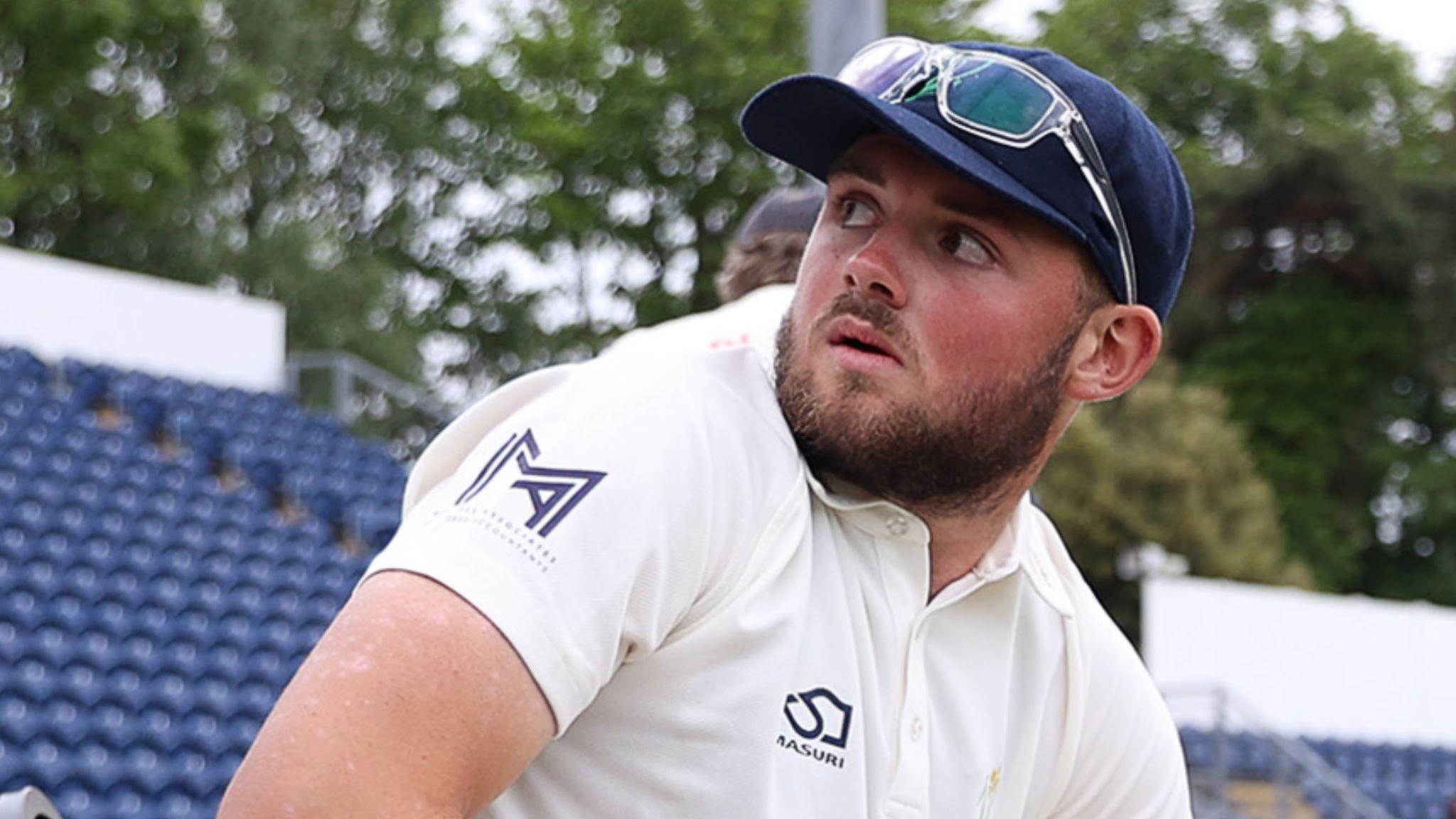 Tom Norton seated on the boundary with glasses on top of cap looks over his shoulder towards the stands at Sophia Gardens