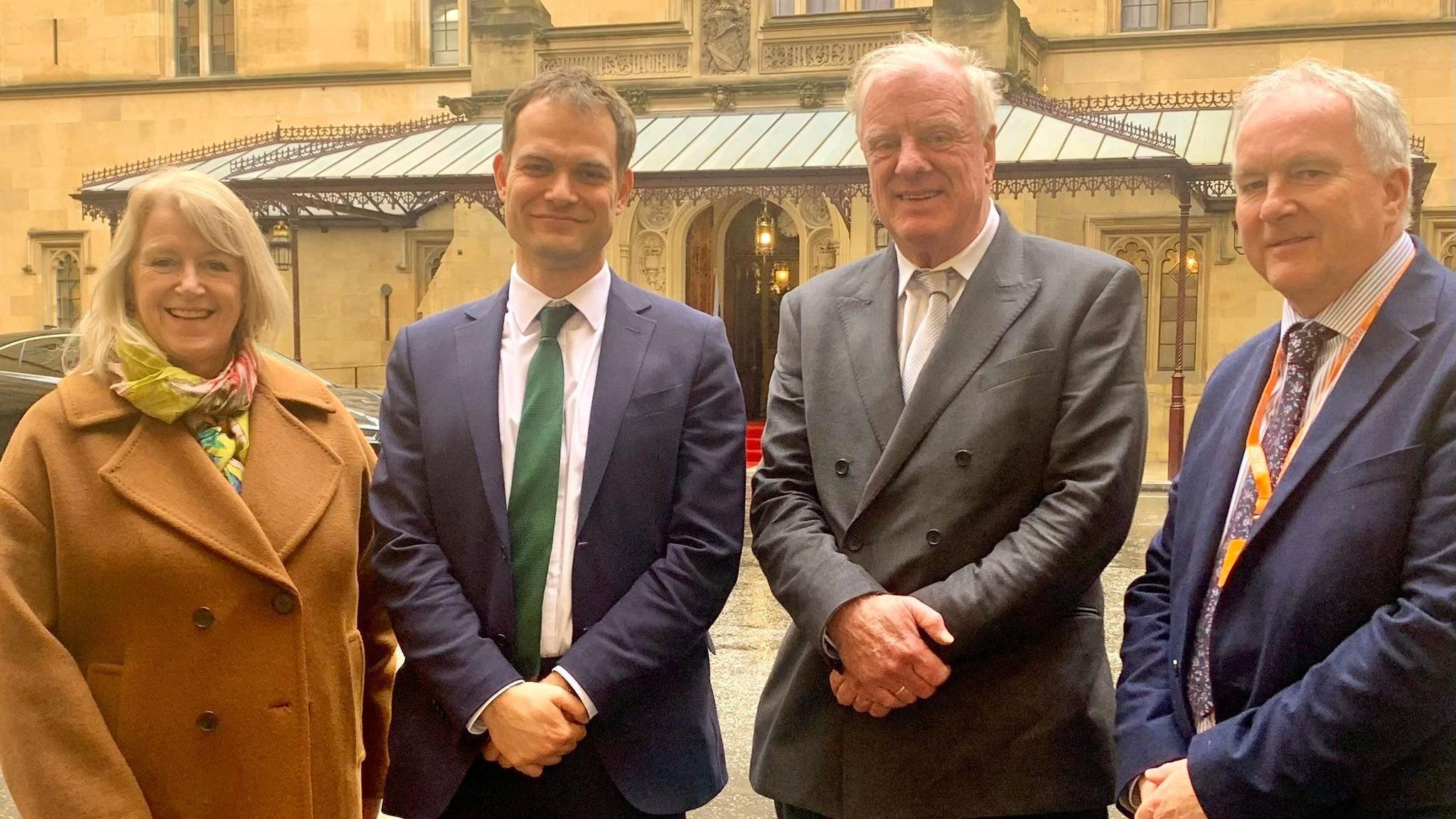 West Lindsey District Council deputy leader Lesley Rollings, Lincoln MP Hamish Falconer, Gainsborough MP Sir Edward Leigh, and council leader Trevor Young smiling and facing the camera outside a building at Westminster. 