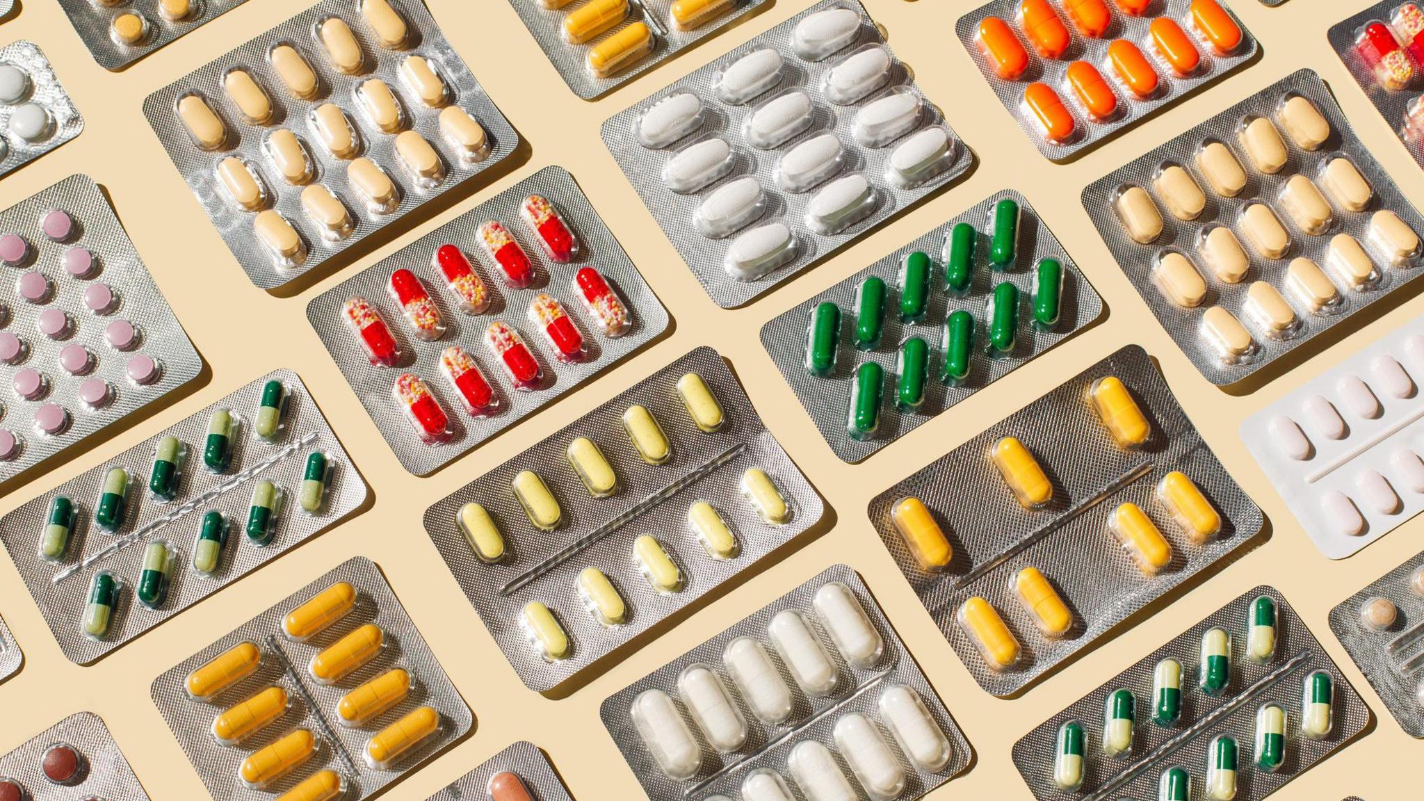 A stock image of many medications laid out in blister packs on a pale-coloured table.
