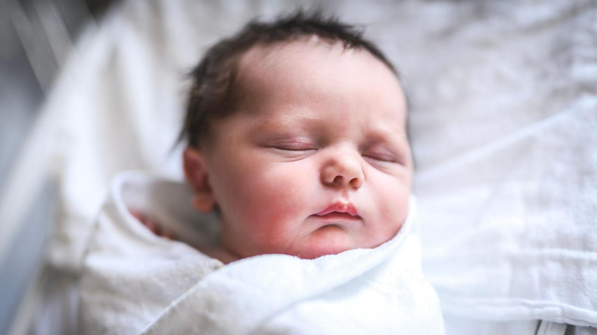 A newborn baby with brown hair in a blankey