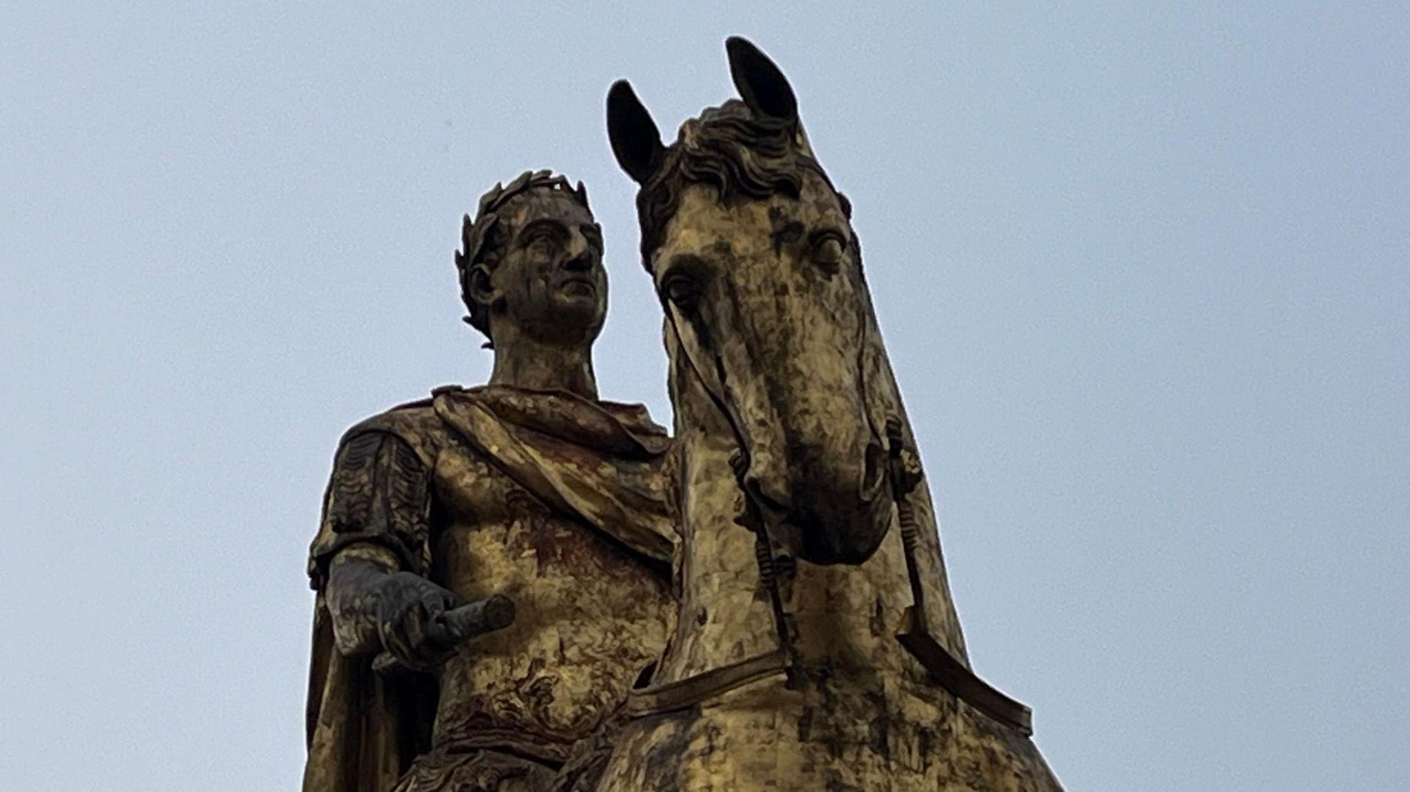 A close up of the face of a statue depicting King William III as he sits astride a horse. The gold gilt covering has tarnished and looks as though it has completely fallen off.