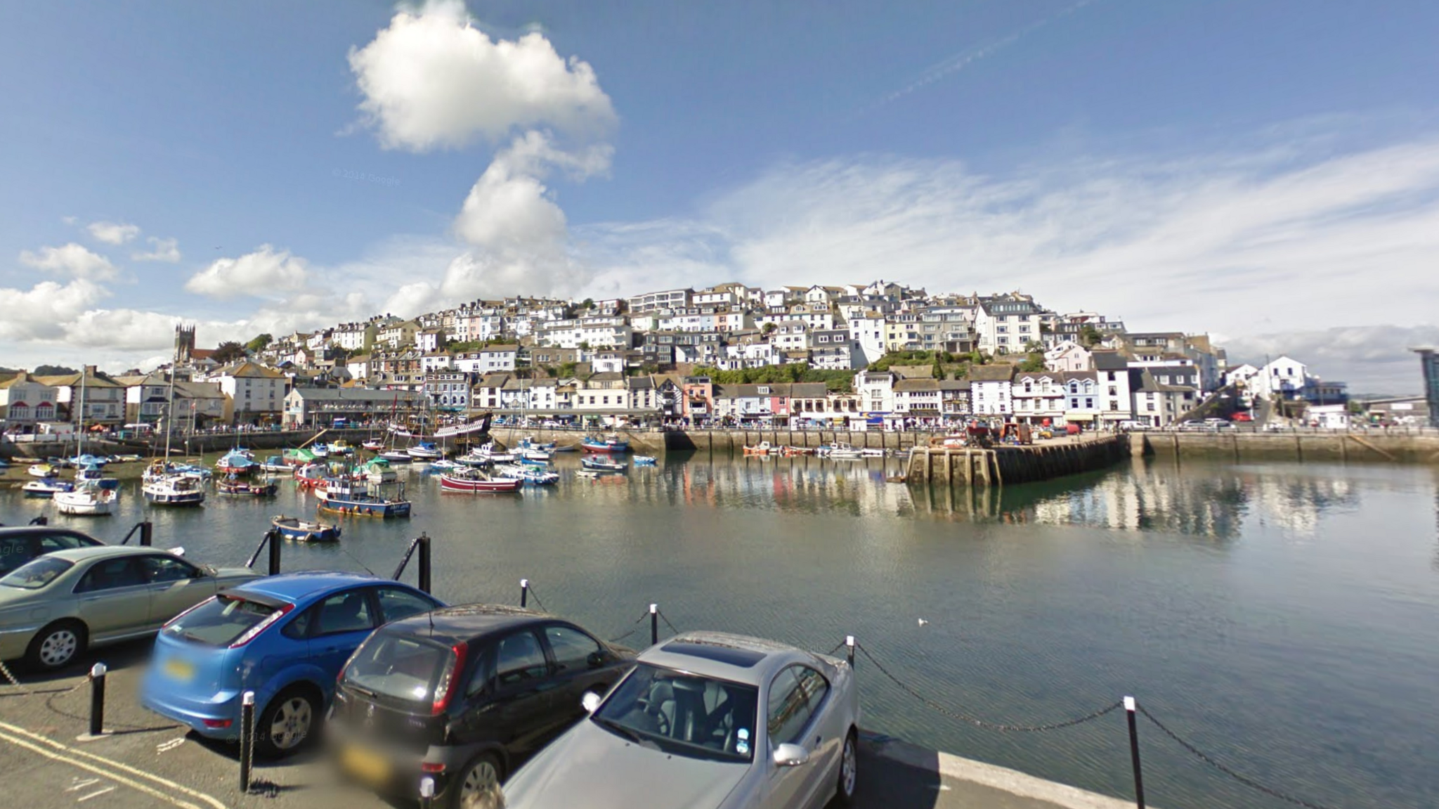 Brixham Harbour, with a number of boats in the harbour and the town rising on a hill behind it