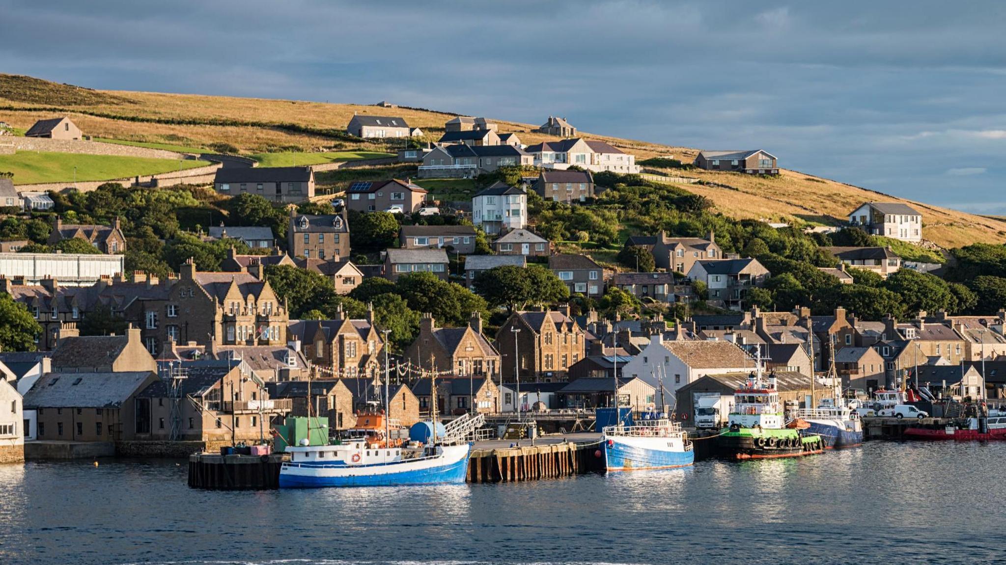A picturesque village, Stromness in Orkney, with boats in the harbour and houses rising up the hillside