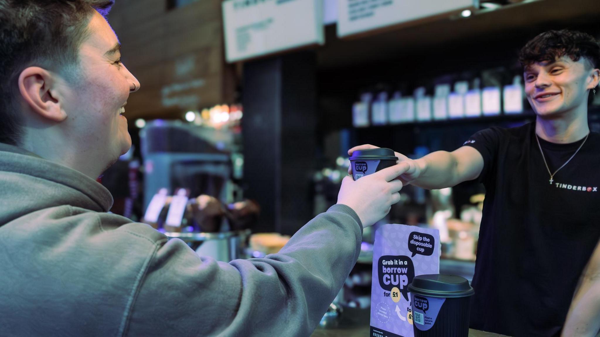 A person handing another person a reusable cup across a bar.