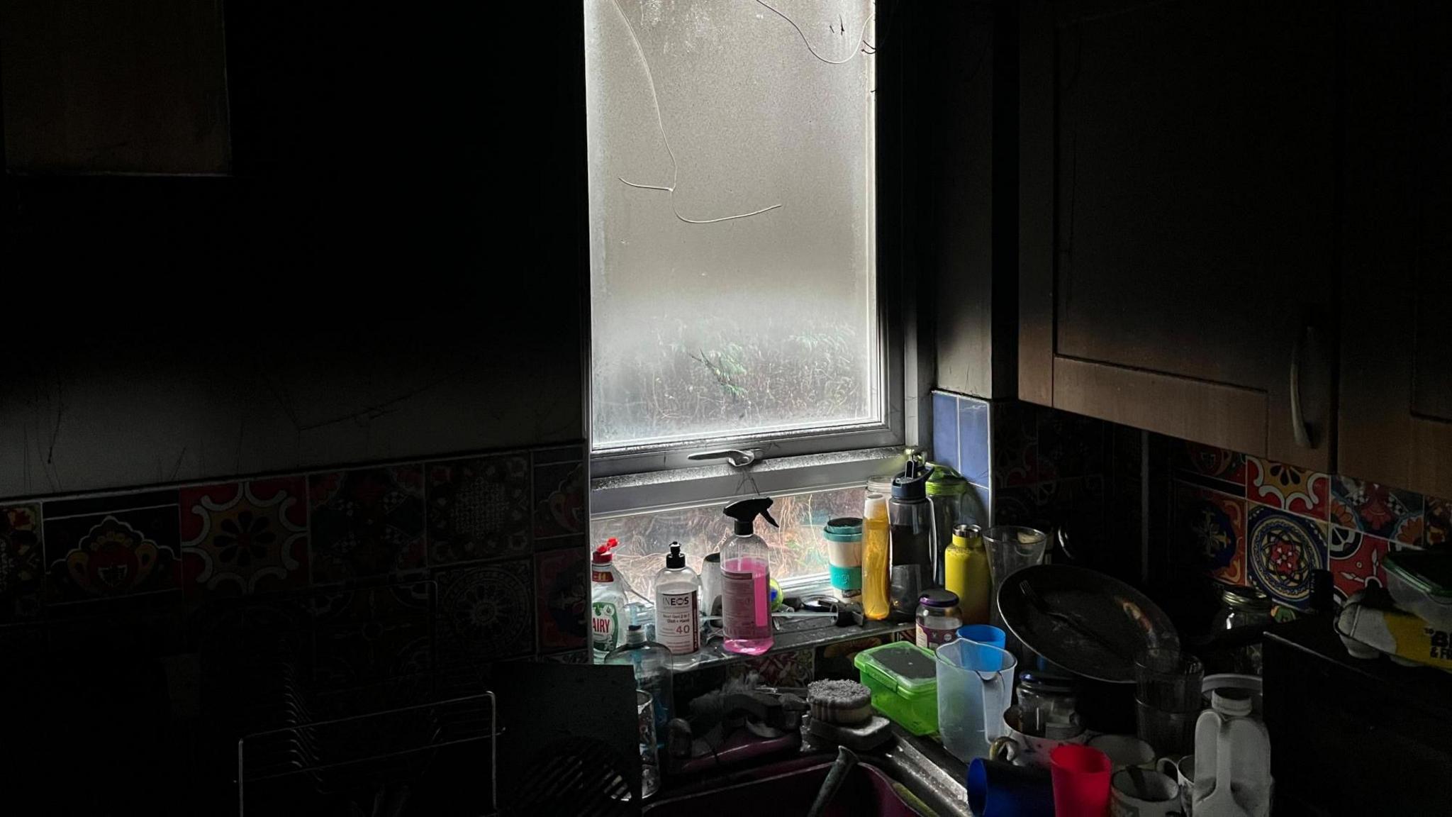 A kitchen sink with cleaning products are all covered in black soot