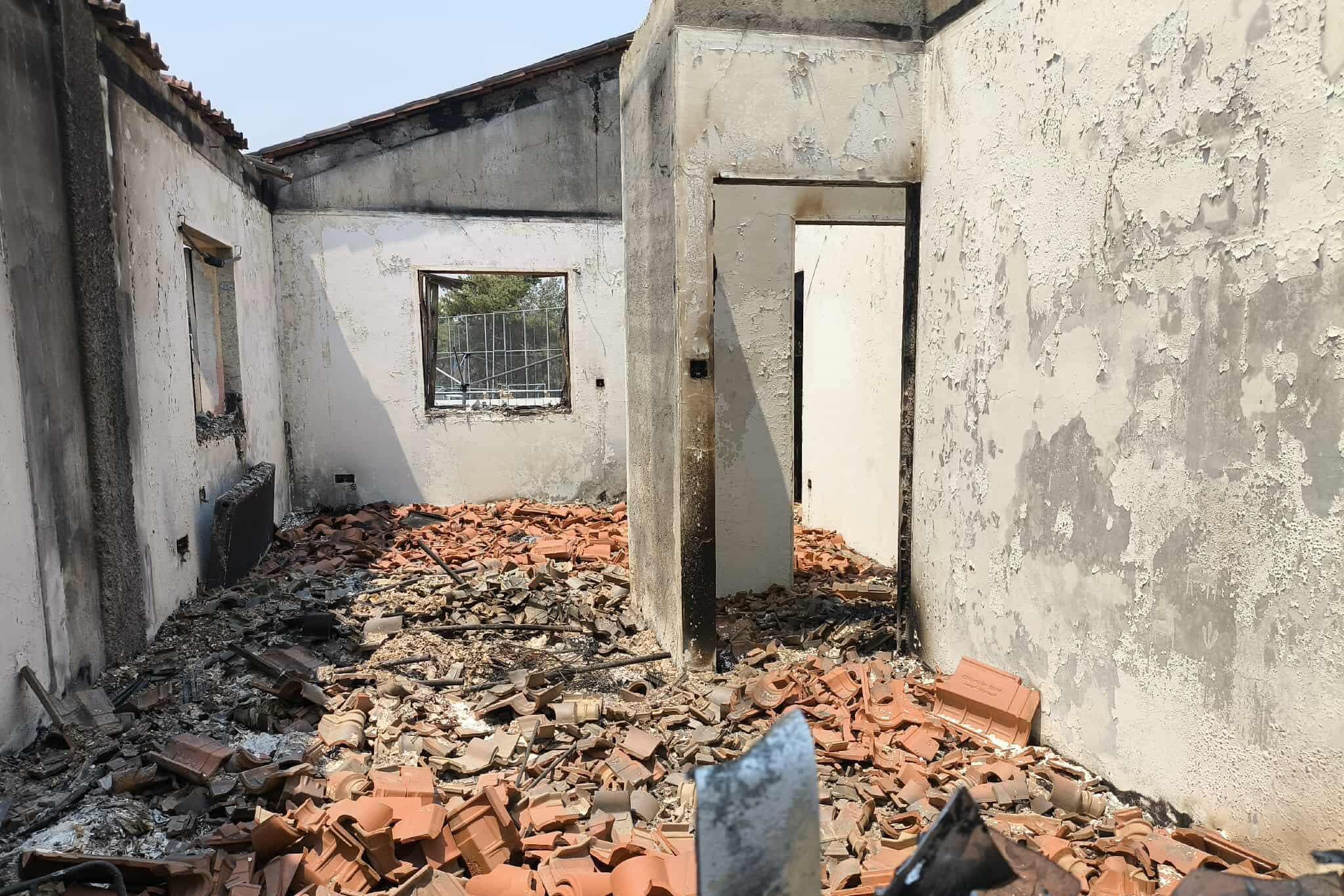 A room in the home showing the extent of the damage. There is no roof on the room and the floor is completely covered in brick and rubble. Ash covers the walls, the windows are completely smashed through. 