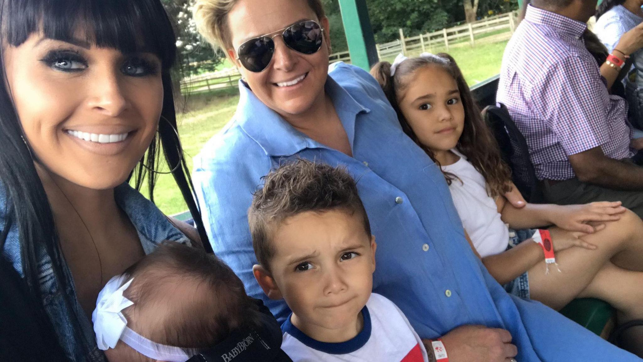 Laura-Rose and her partner sit, smiling, on a bench with grass in the background with three of their children