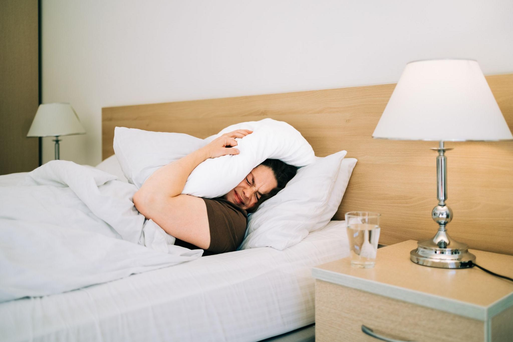 Woman lying in bed with a pillow over her head