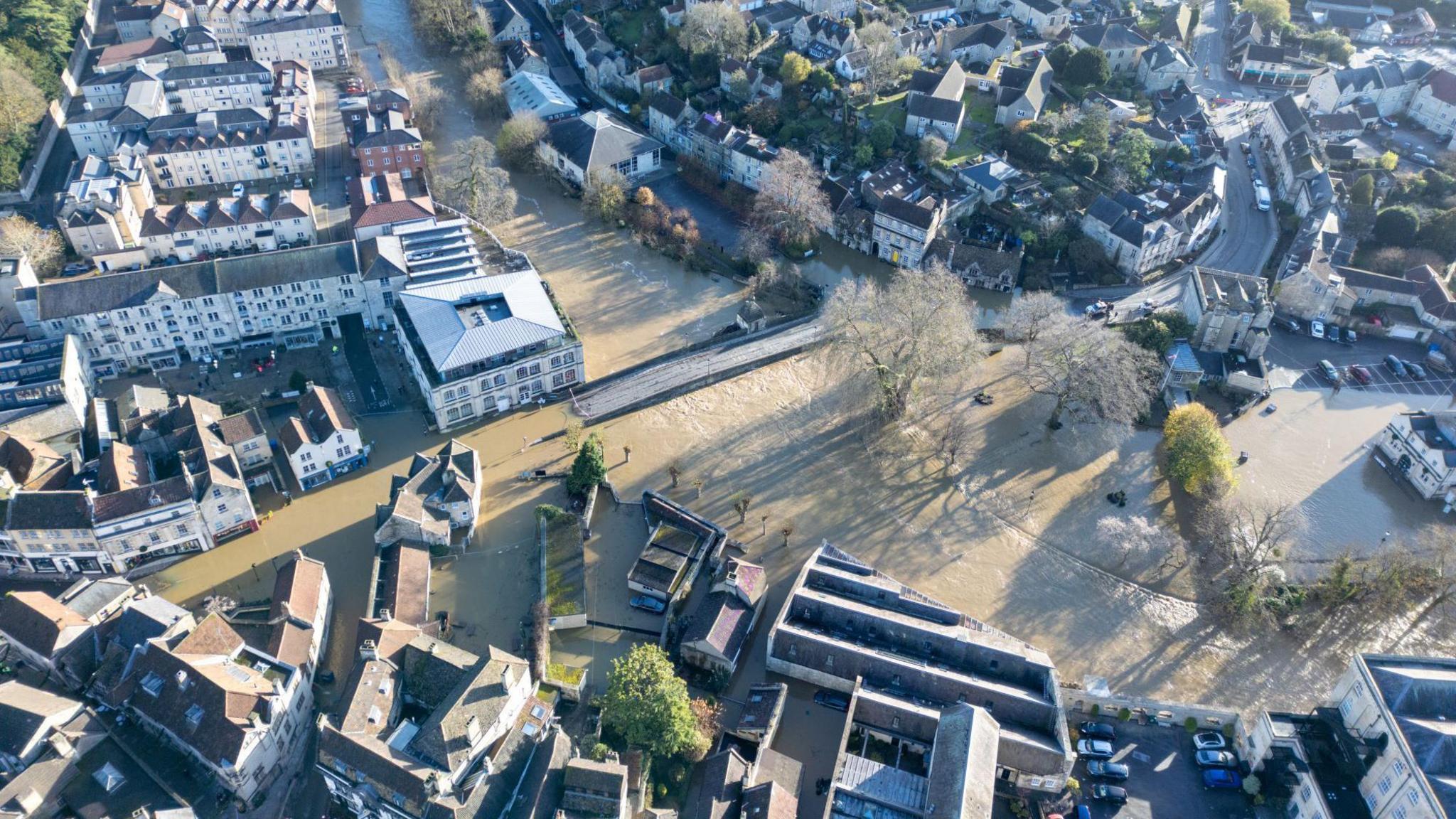 The centre of Bradford-on-Avon is seen from a drone, with many streets underwater after Storm Bert. The floodwaters are a pale brown colour and in the centre of the image the Town Bridge can be seen almost covered in the water