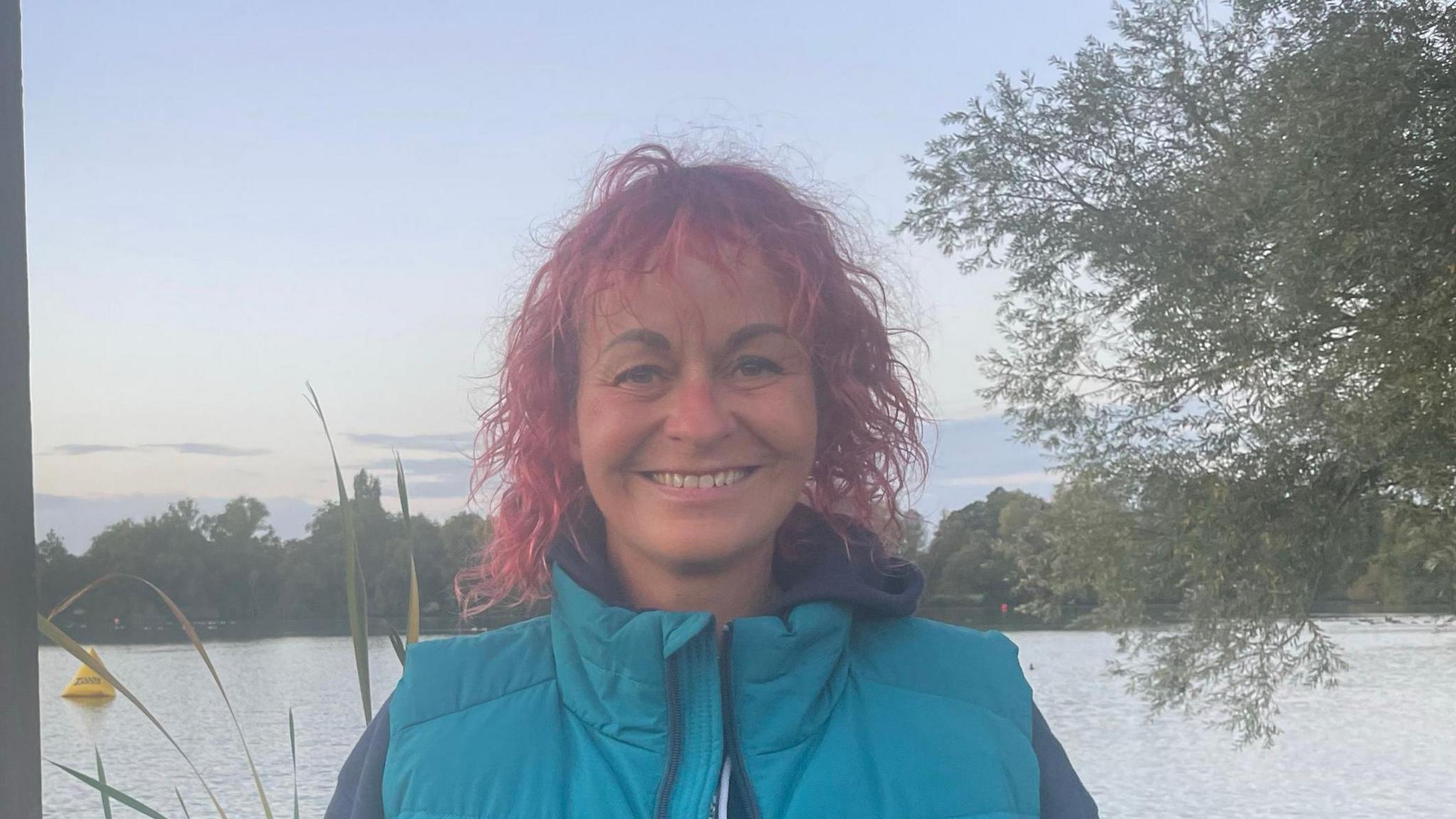 A smiling woman stands in front of the lake