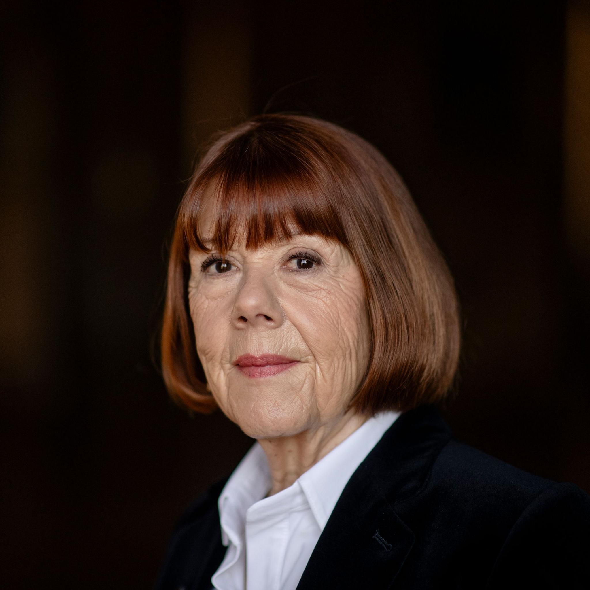 Gisèle Pelicot, a woman with short grey hair and glasses, looks thoughtfully into the distance, wearing a dark jacket.