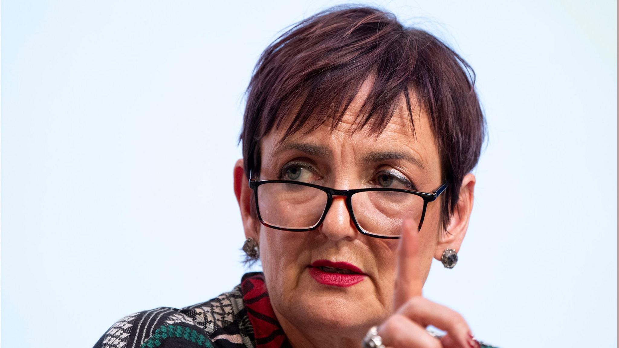 Angela Constance, wearing dark-framed glasses, looking to the side with her finger raised