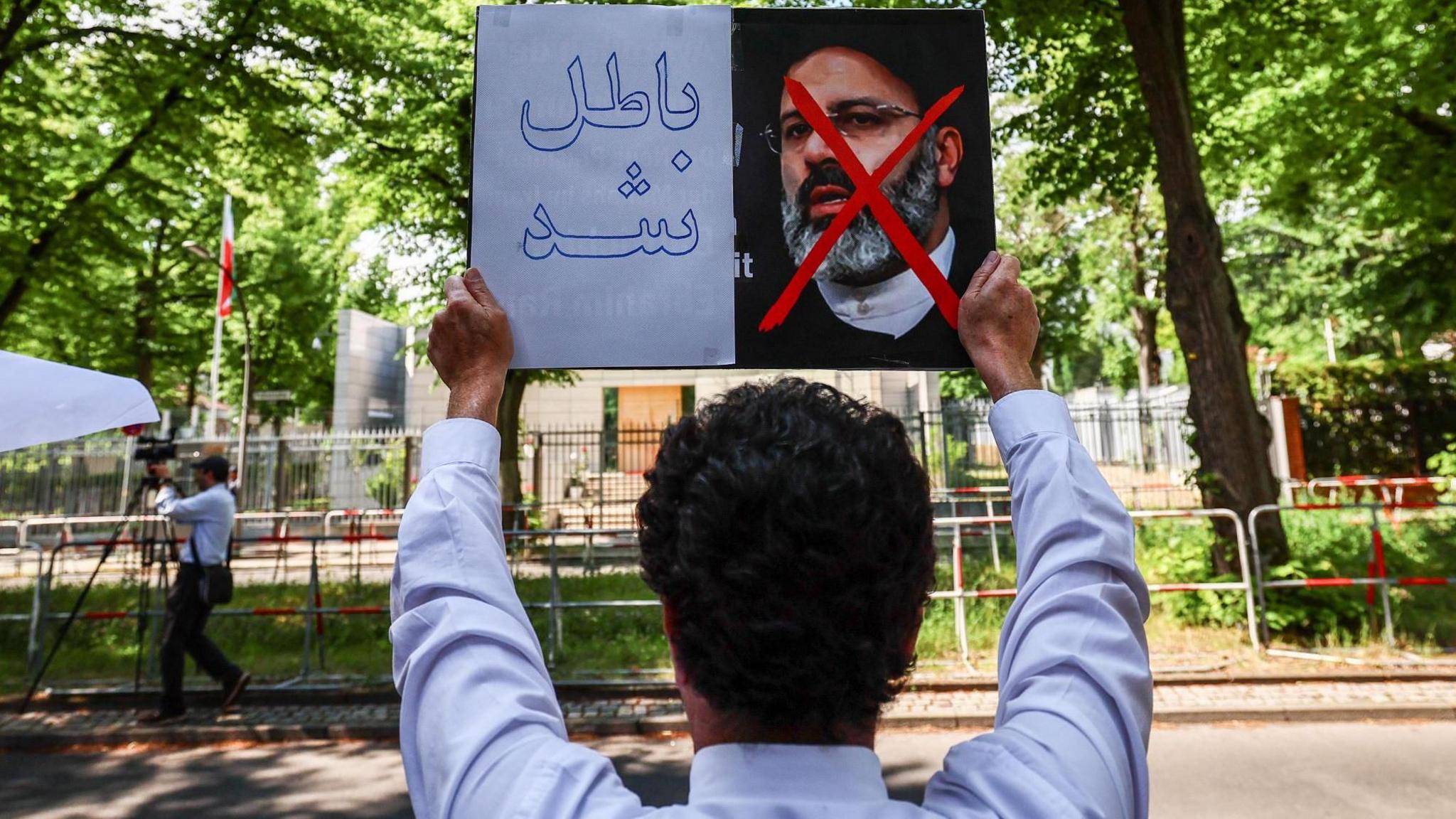 Person holding placard with a picture of the president under a red cross