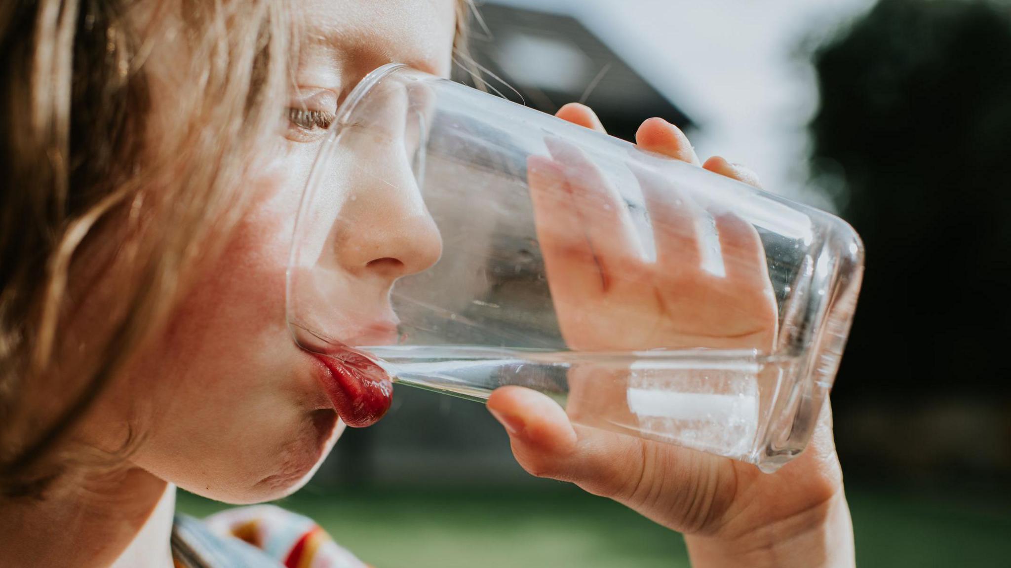 A little girl drinks a refreshing glass of water outside, on a sunny day. - stock photo