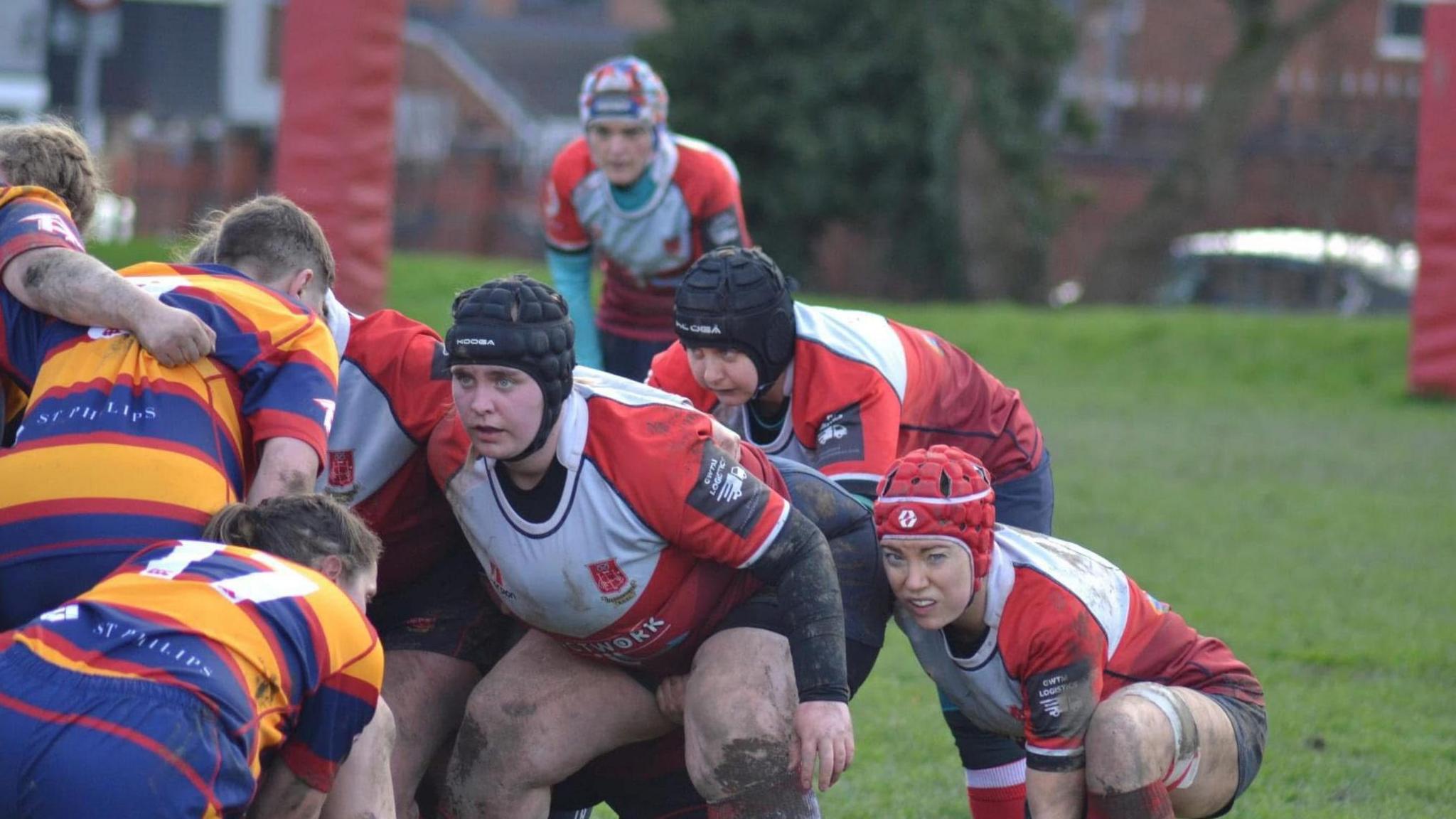 A rugby scrum with women in red and white outfits covered in mud.