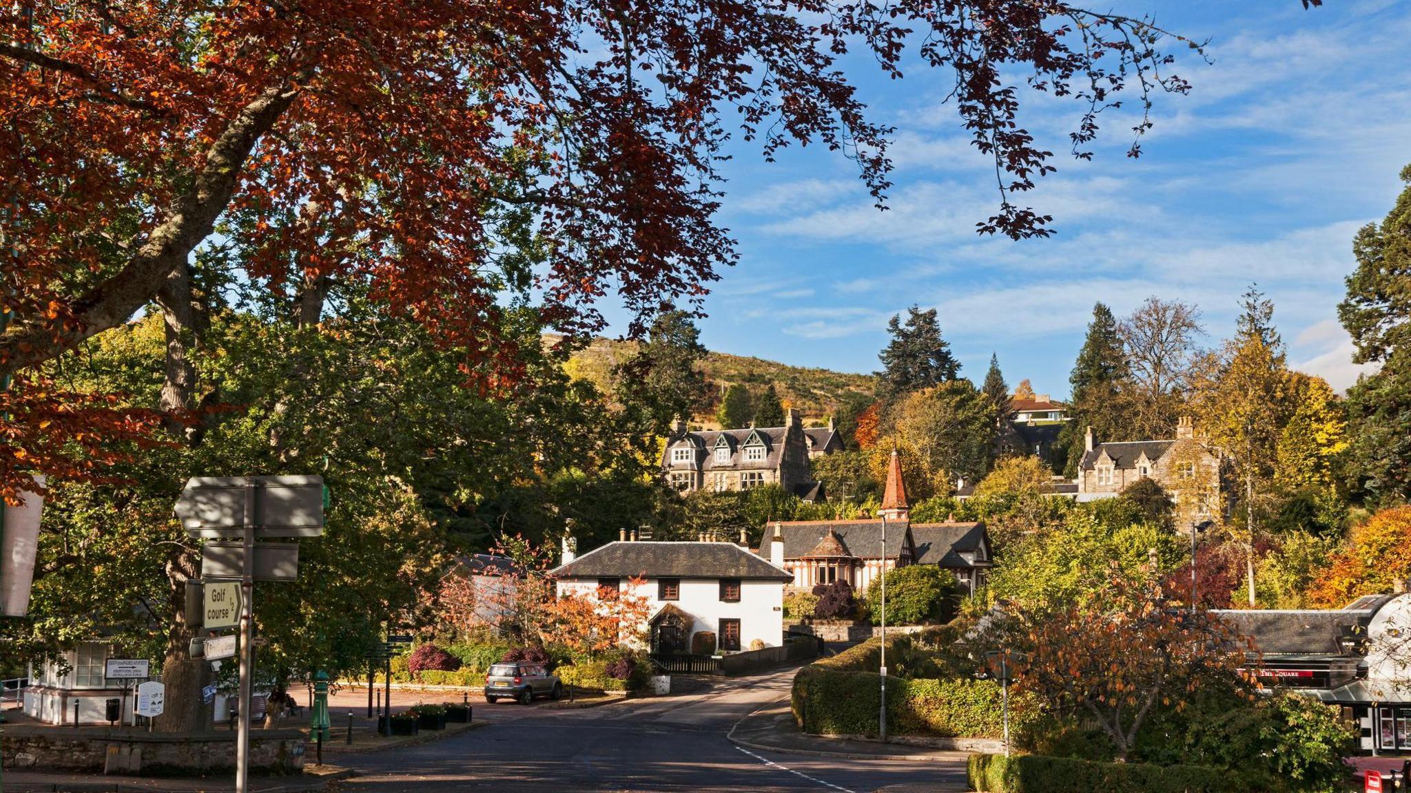 The Victorian heart of the Highland village of Strathpeffer. There are lots of trees and a hill in the background.