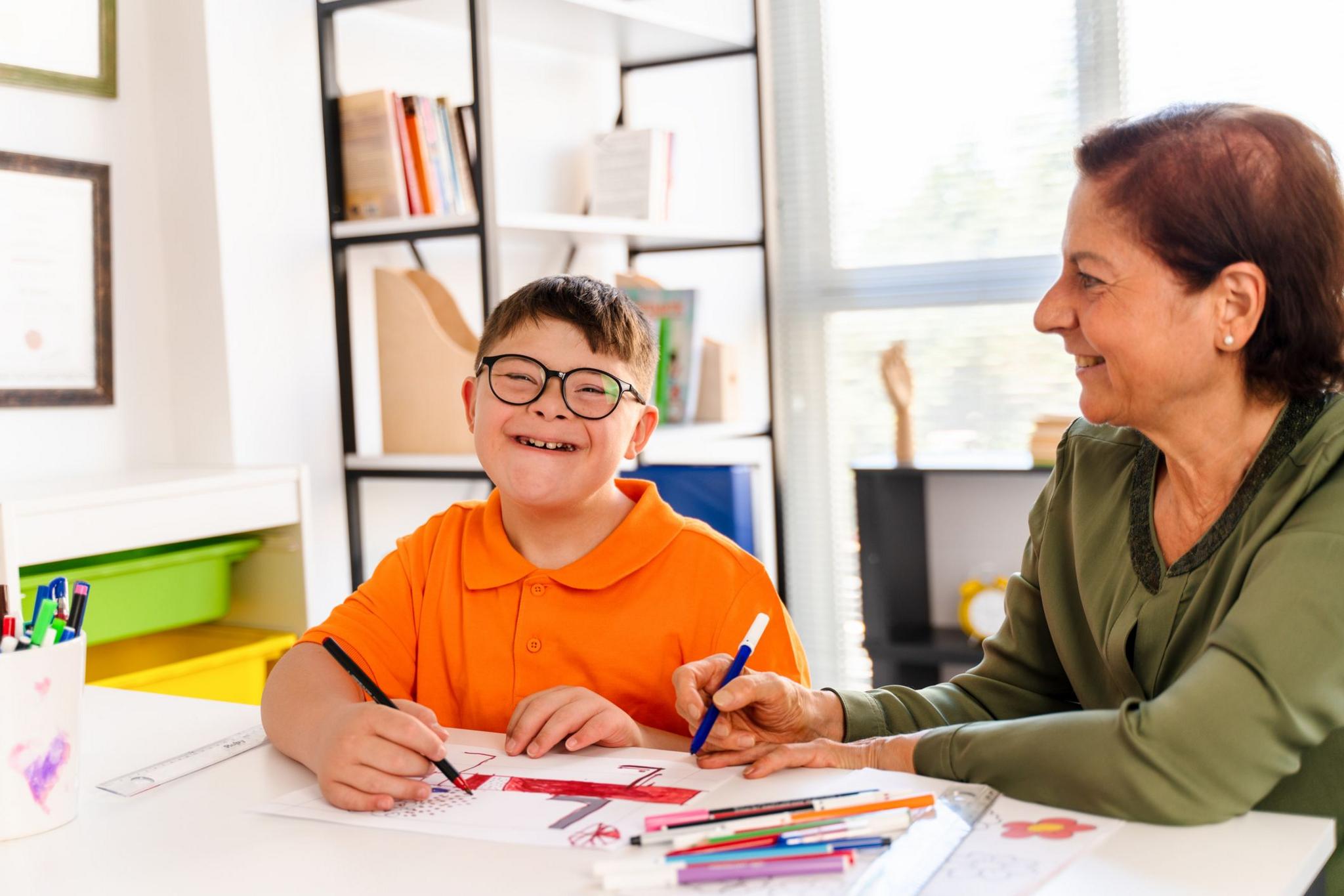 boy smiling and colouring with teacher. 