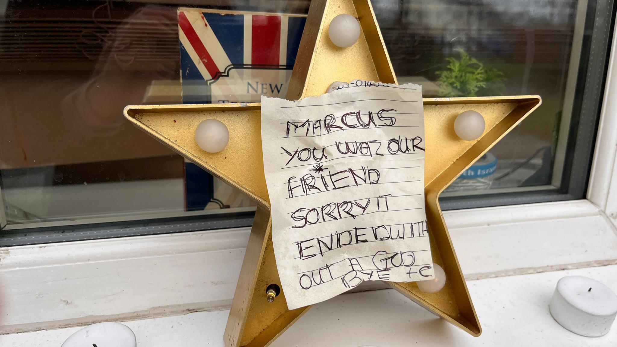 A message was pinned on a star and surrounded by candles on a window ledge. It says: Marcus you was our friend. Sorry it ended without a goodbye. 

