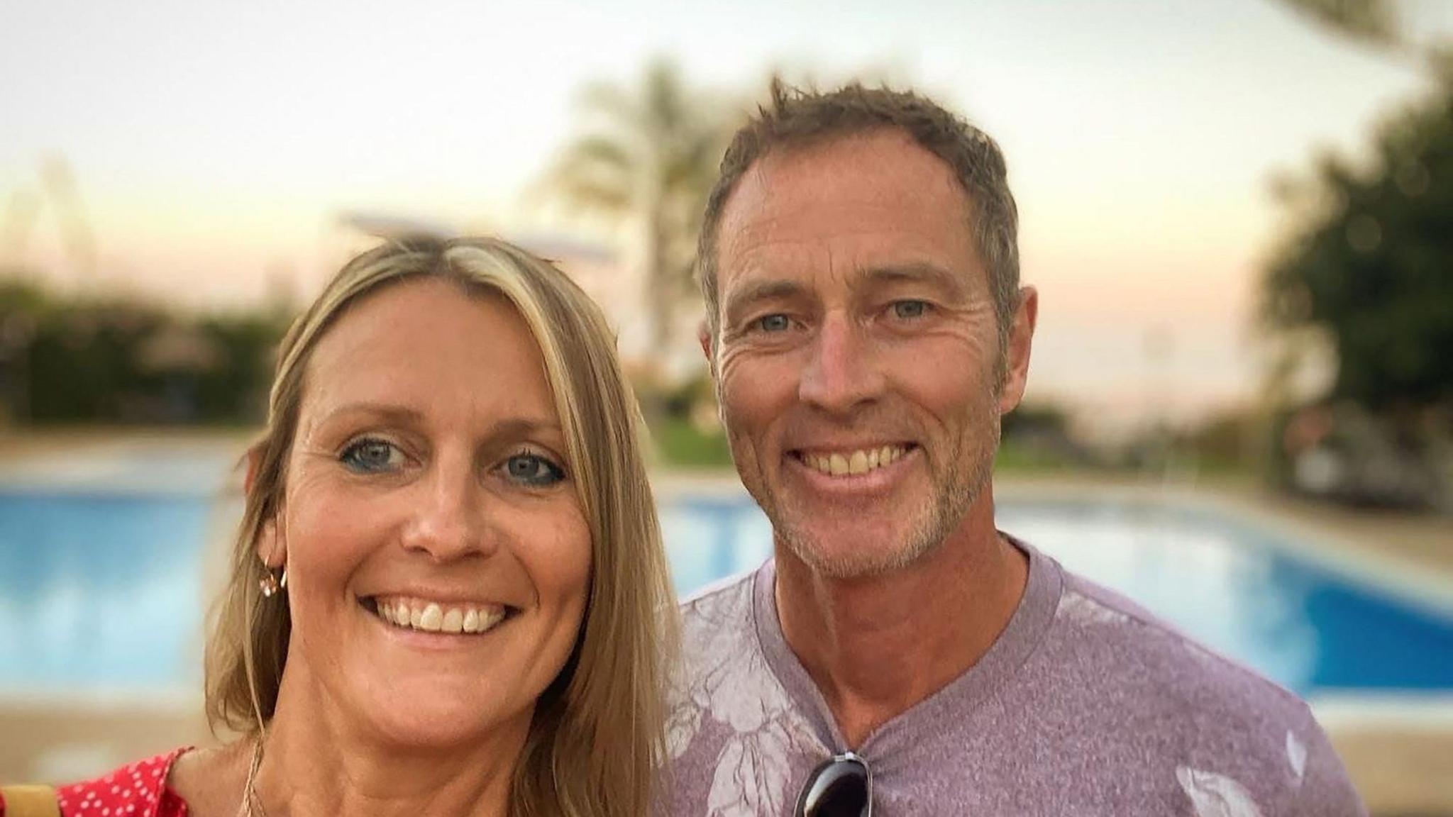 A blonde woman standing next to a man with greying hair. They are at a resort. 